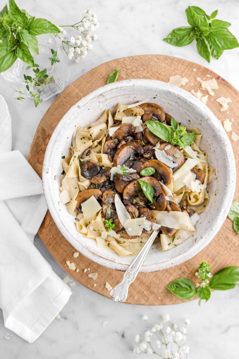 mushroom tagliatelle in large bowl with fork tucked under pasta with cheese and fresh herbs on top.