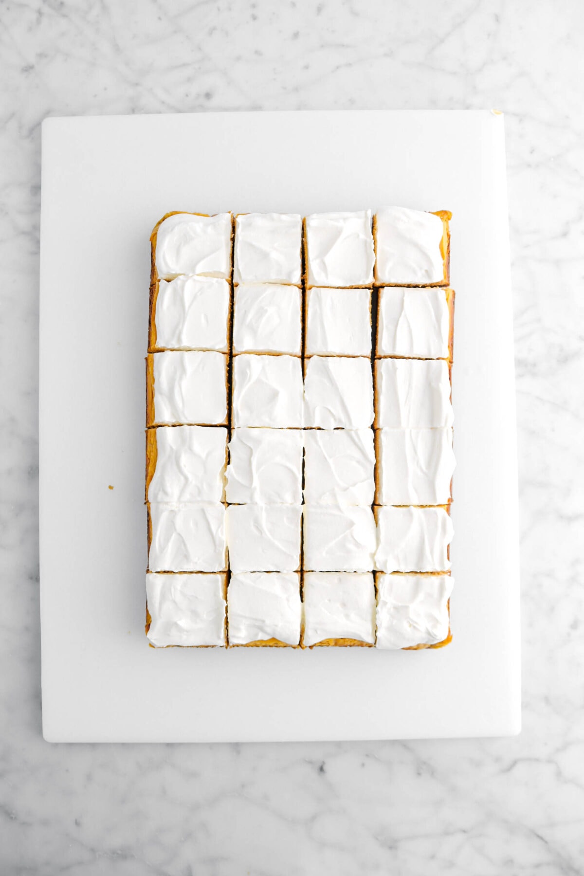 pumpkin cheesecake with whipped cream on top cut into twenty four bars on white cutting board.