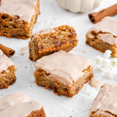 pumpkin spice blondies with icing on top on parchment paper with white pumpkin behind.