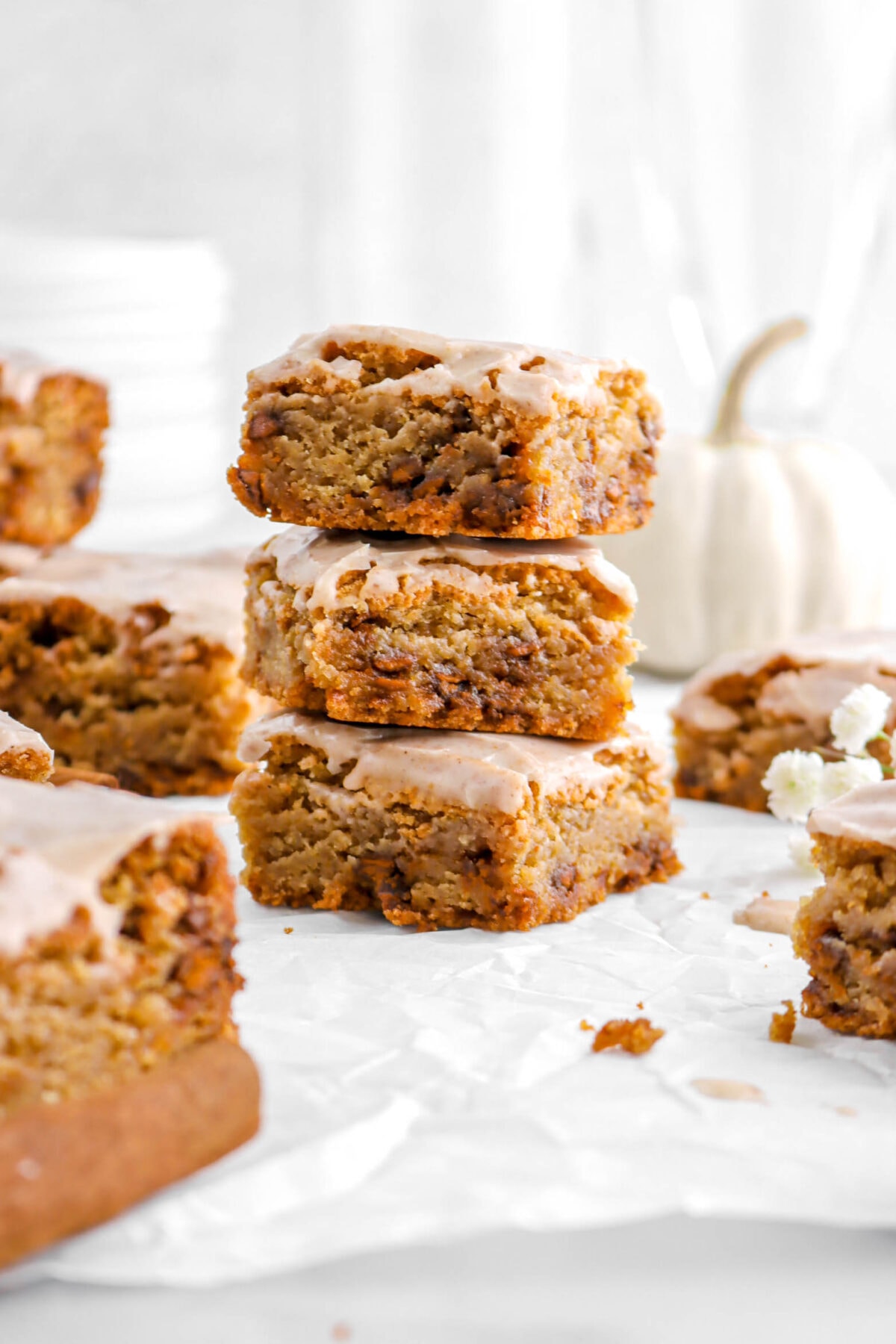 close up of three stacked pumpkin spice blondies on parchment paper with more blondies around.