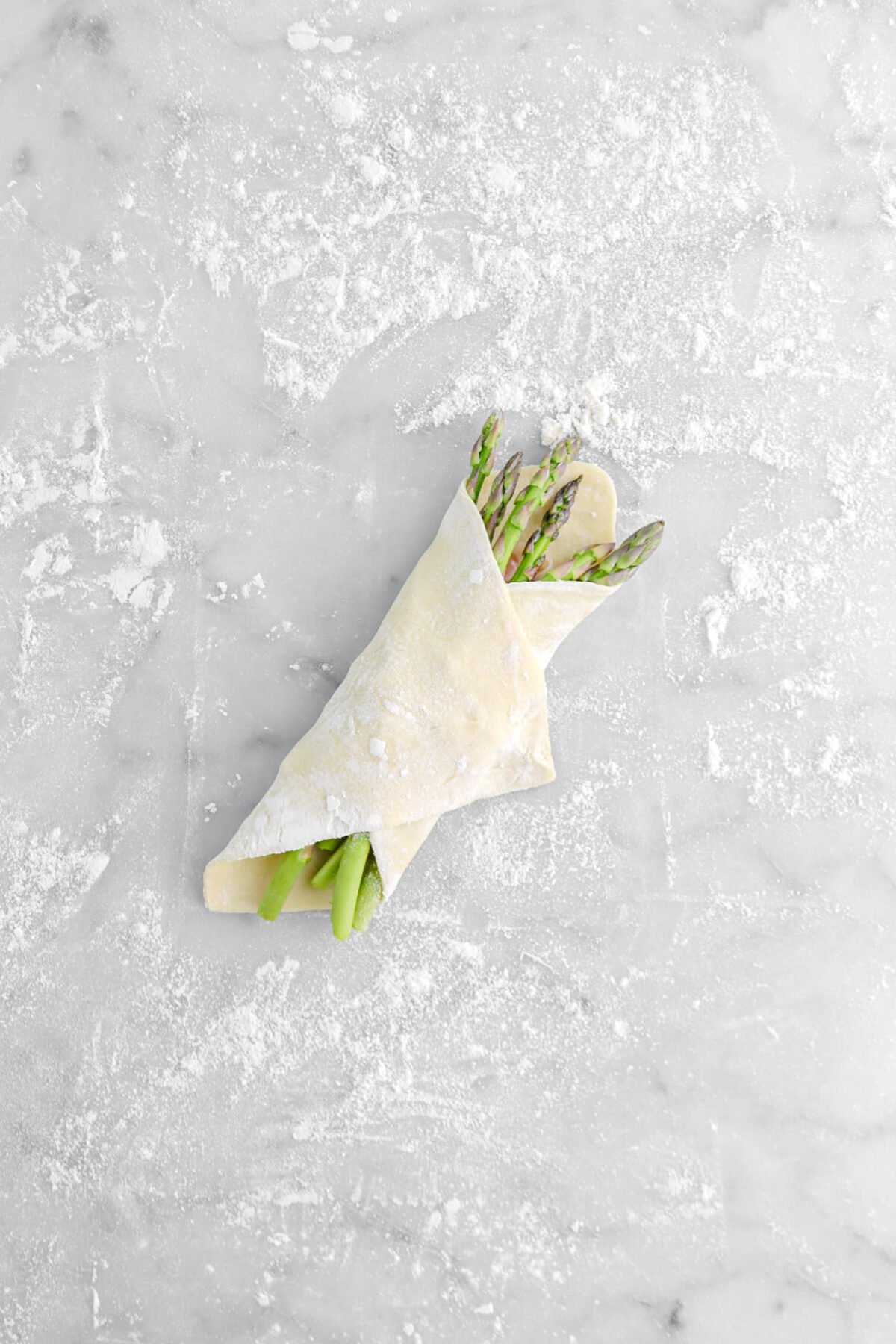 puff pastry wrapped around asparagus on marble surface.