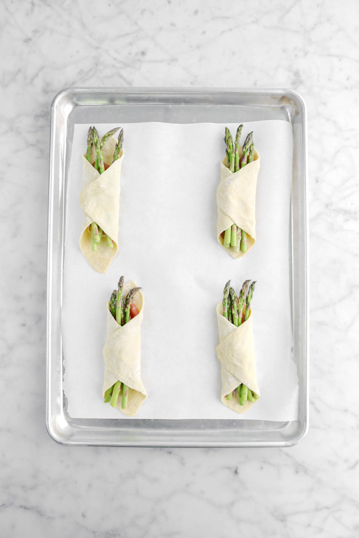 four asparagus bundles on parchment lined sheet pan.