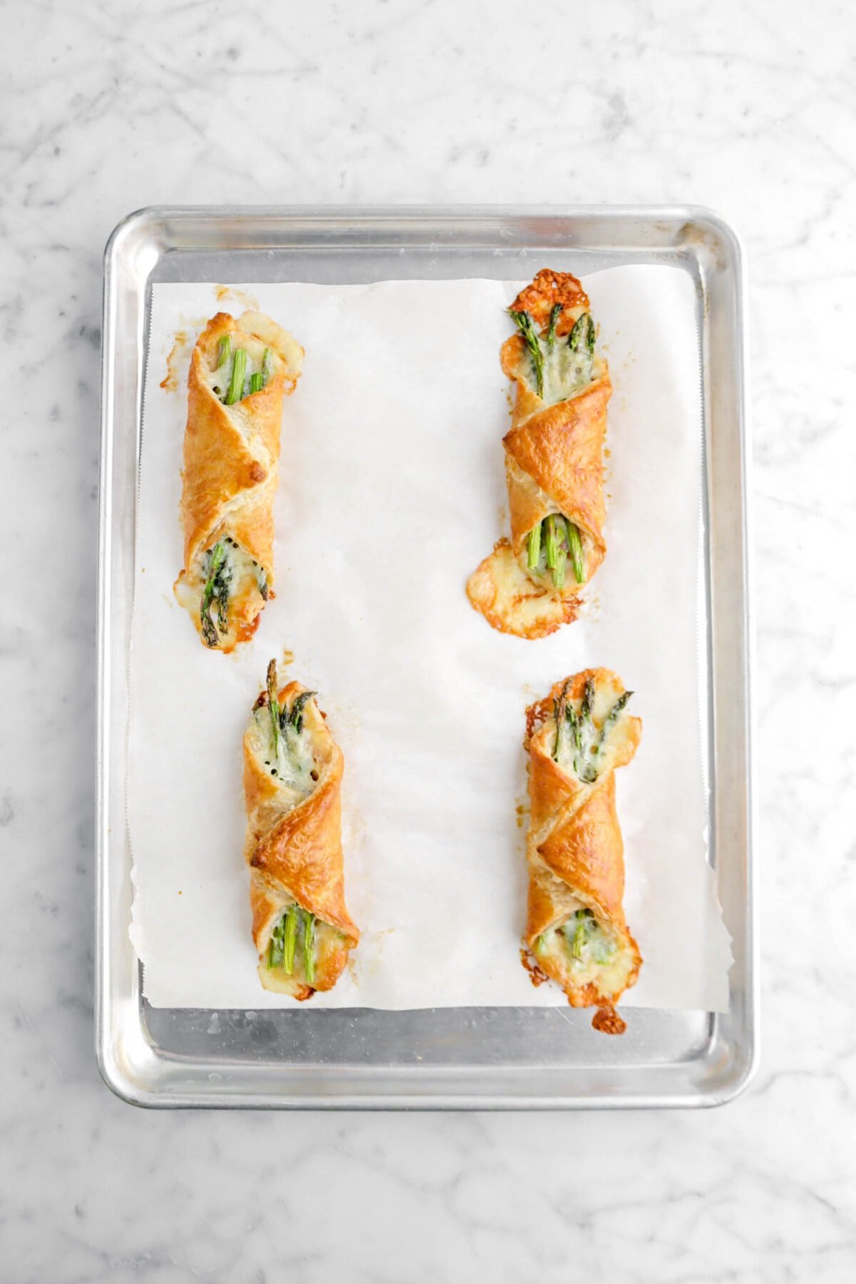 four baked asparagus bundles on lined sheet pan.