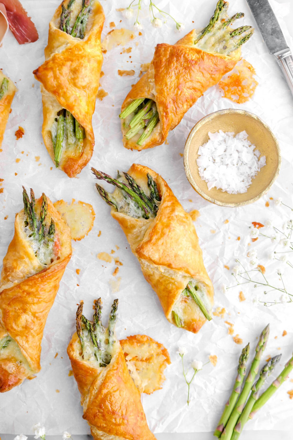 pastry bundles on parchment paper with fresh asparagus and flowers around.