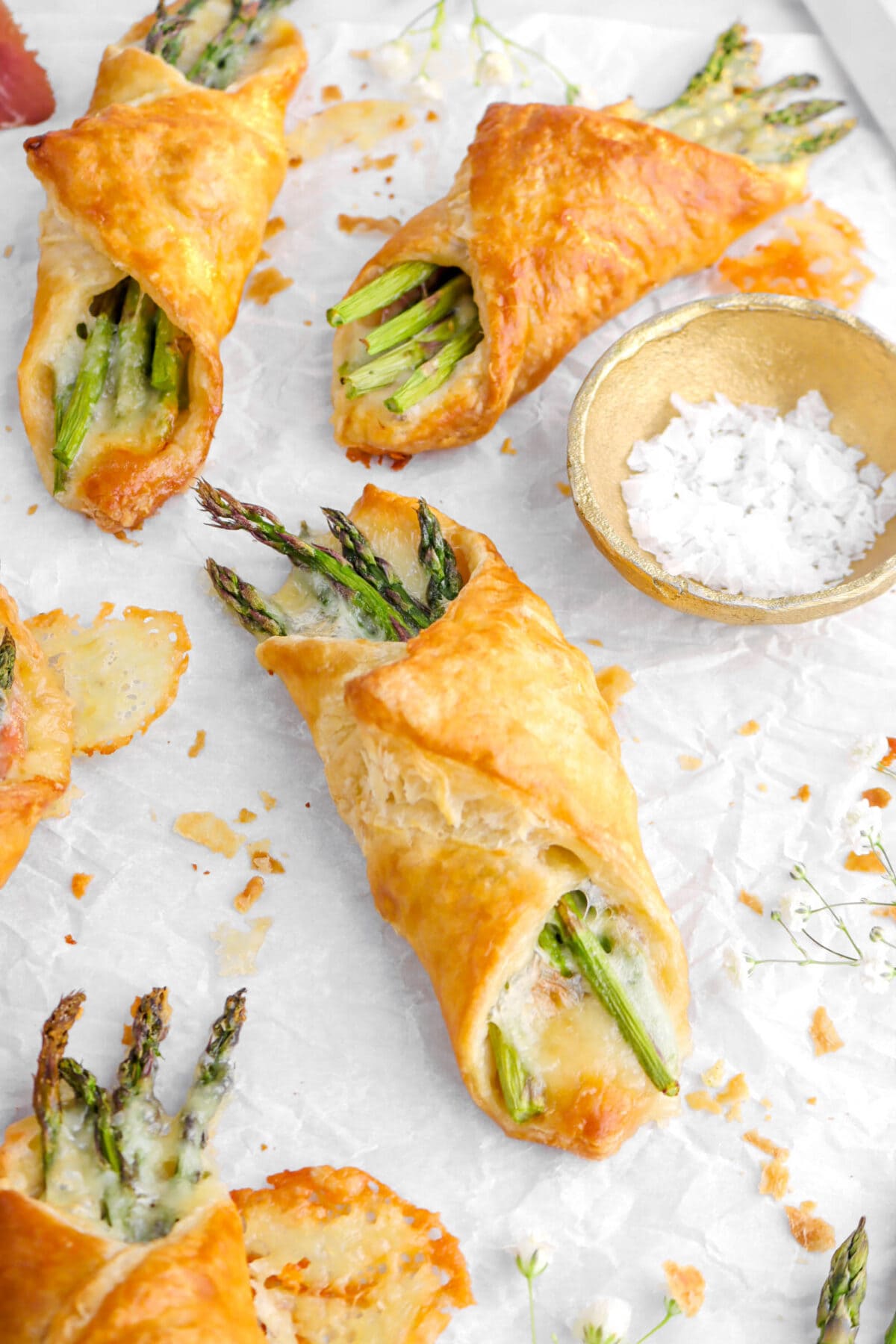 angled shot of asparagus pastry bundle with two more behind on parchment paper.