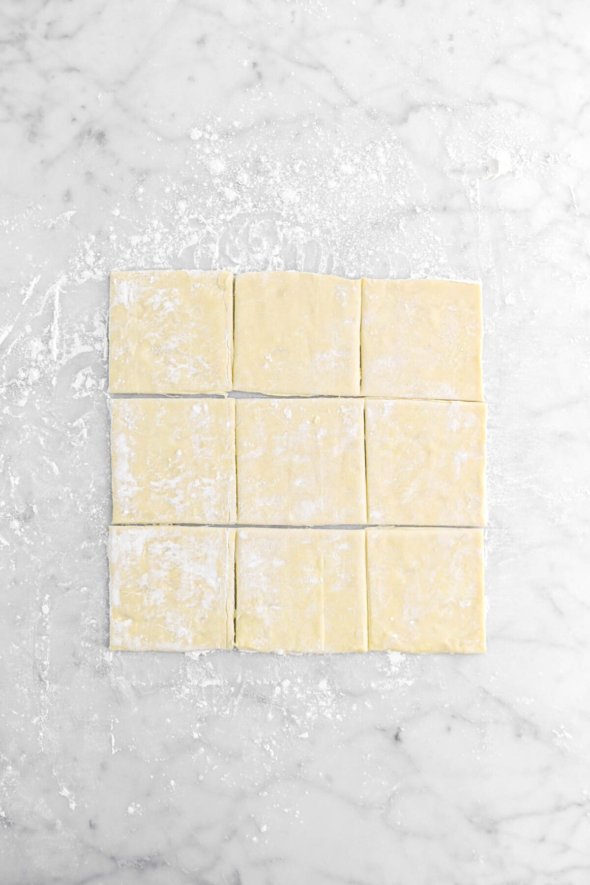 nine small squares of puff pastry on marble surface.