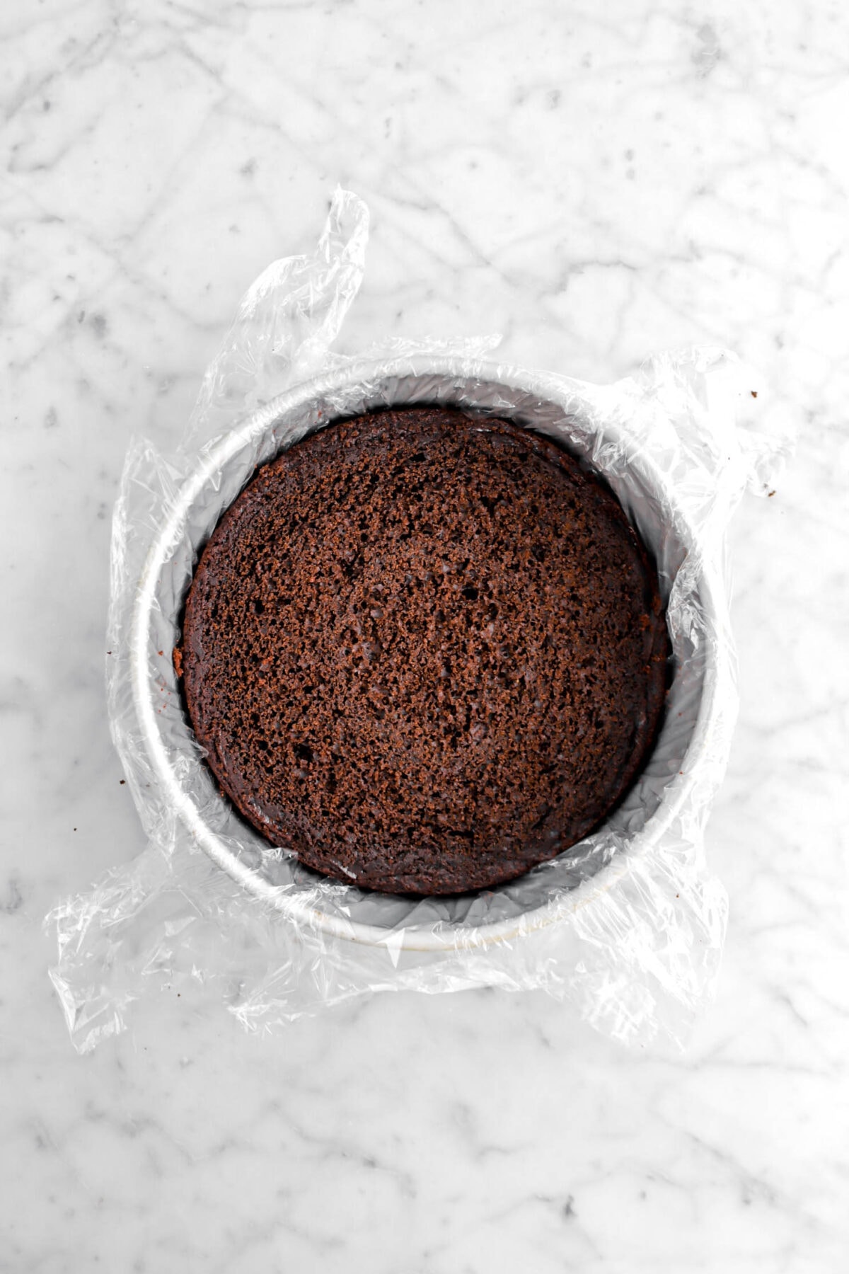 leveled chocolate cake in plastic wrap lined cake pan.
