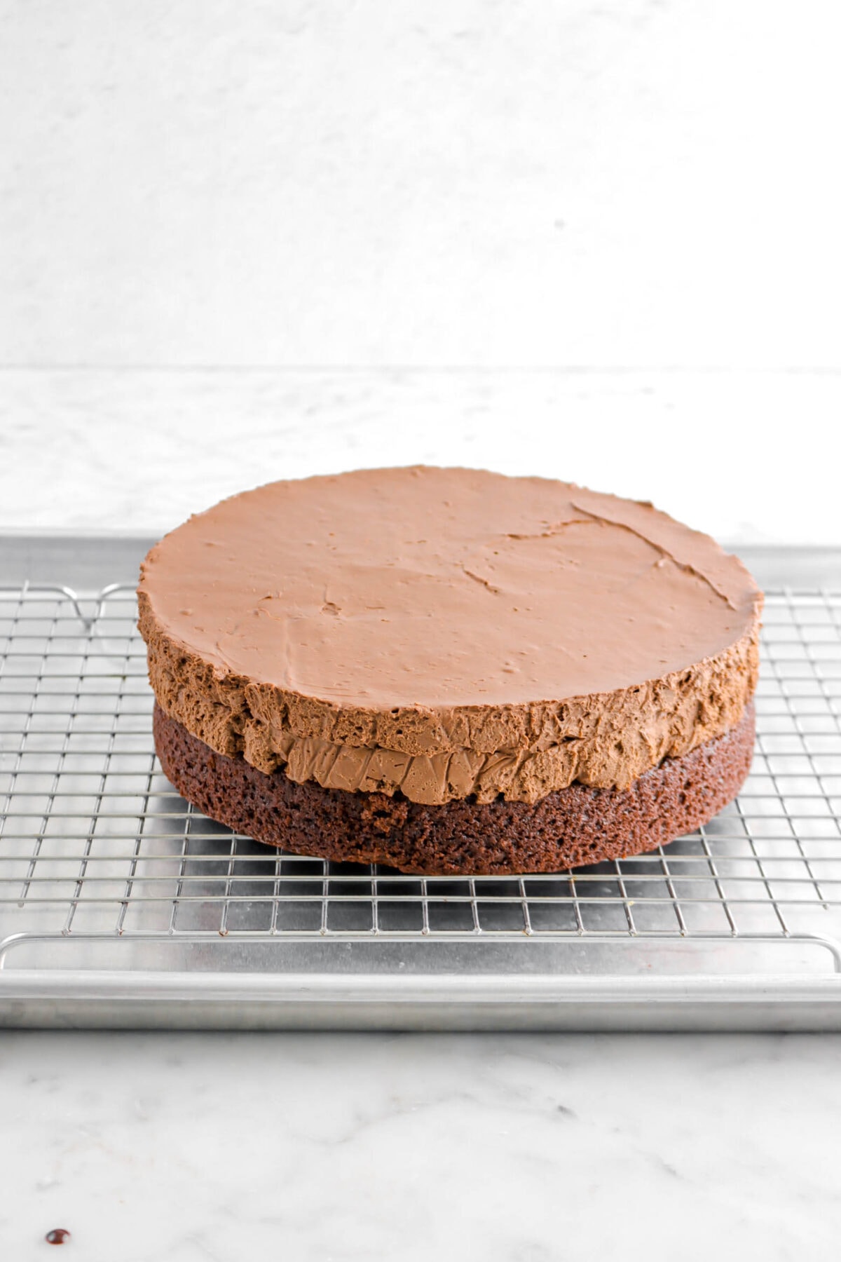 chocolate cake with mousse on top on a cooling rack lined sheet pan.