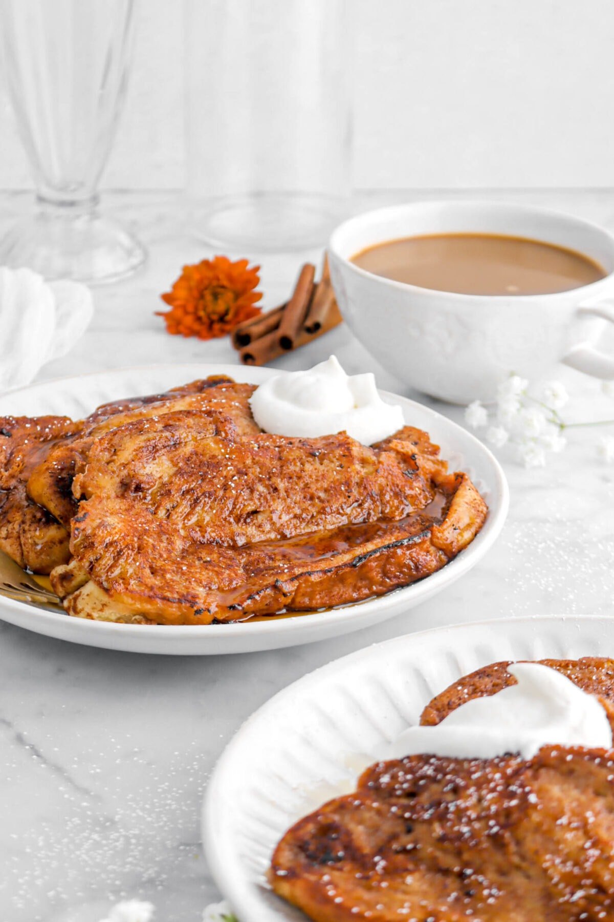 cropped front shot of french toast on two white plates and mug of coffee behind.