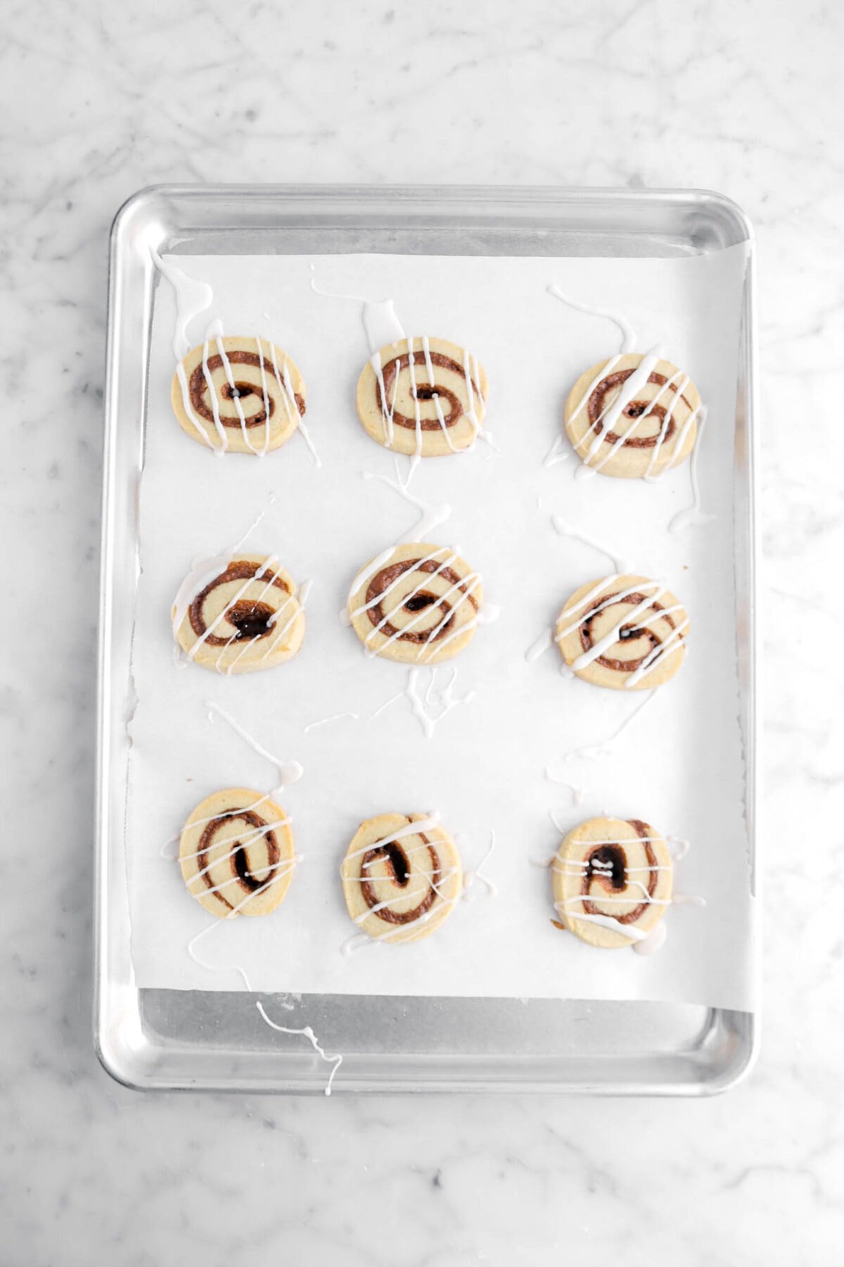 baked cinnamon roll cookies on sheet pan with icing drizzled over the top.