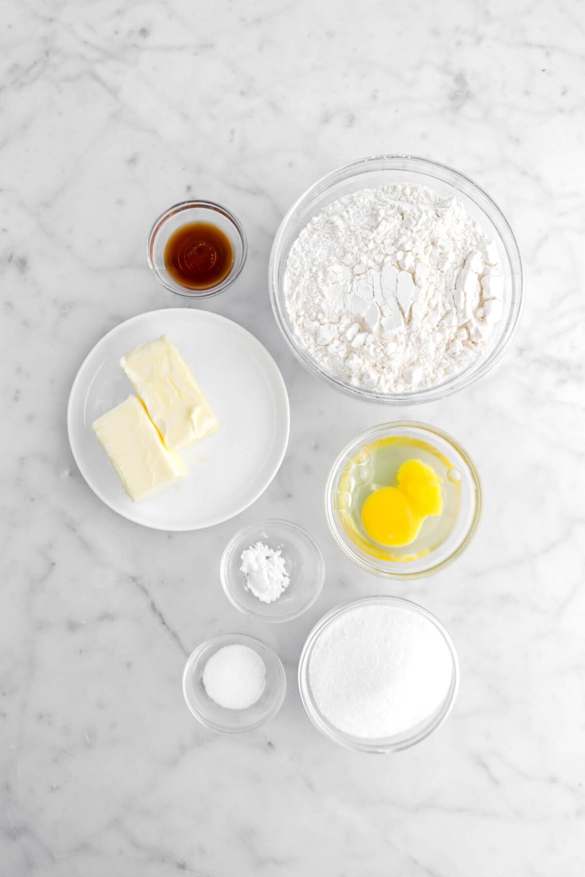vanilla, butter, flour, egg, baking powder, salt, and sugar on marble surface.