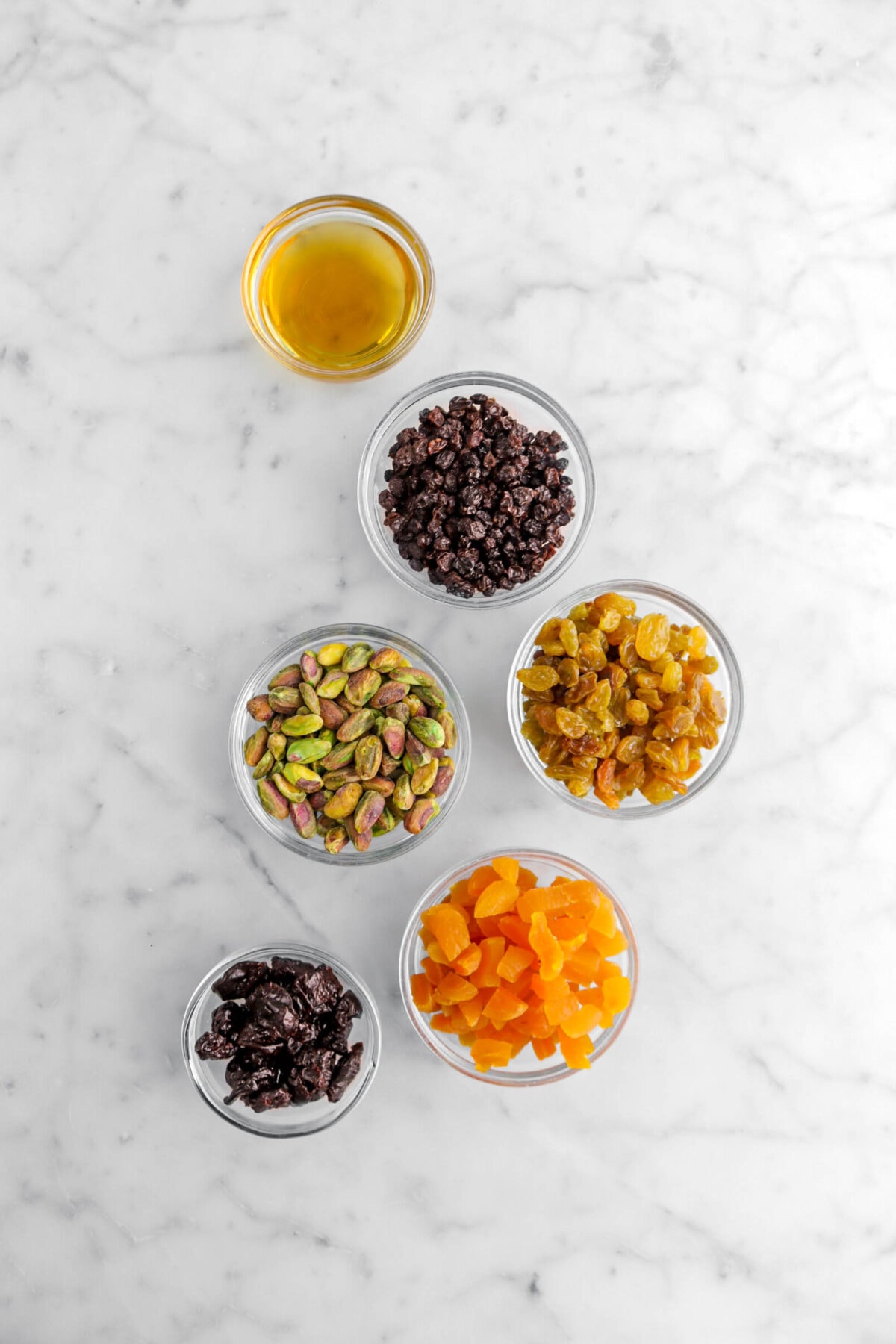 rum, dried currants, golden raisins, pistachios, dried cherries, and dried apricots on marble surface.