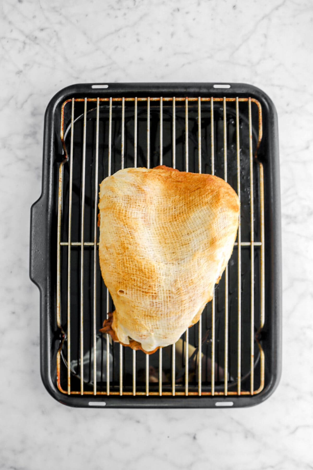 baked turkey breast wrapped in cheesecloth on roasting pan.