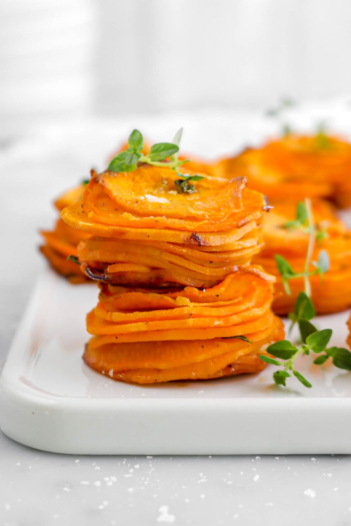 close up of two sweet potato stacks stacked on each other with thyme sprig beside and on top, with more sweet potato stacks behind.
