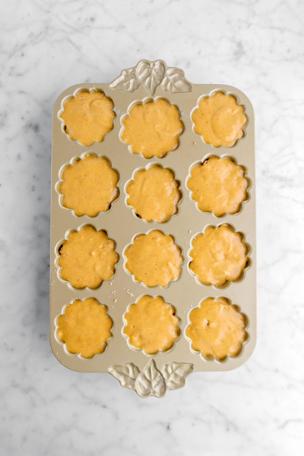 cake batter in twelve pumpkin shaped cavity's in gold pan.