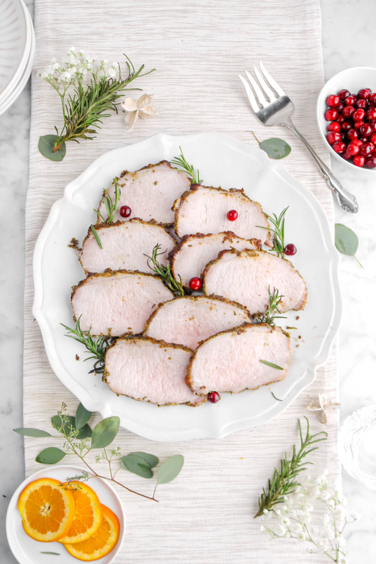 nine slices of pork on round platter with rosemary sprigs and cranberries.