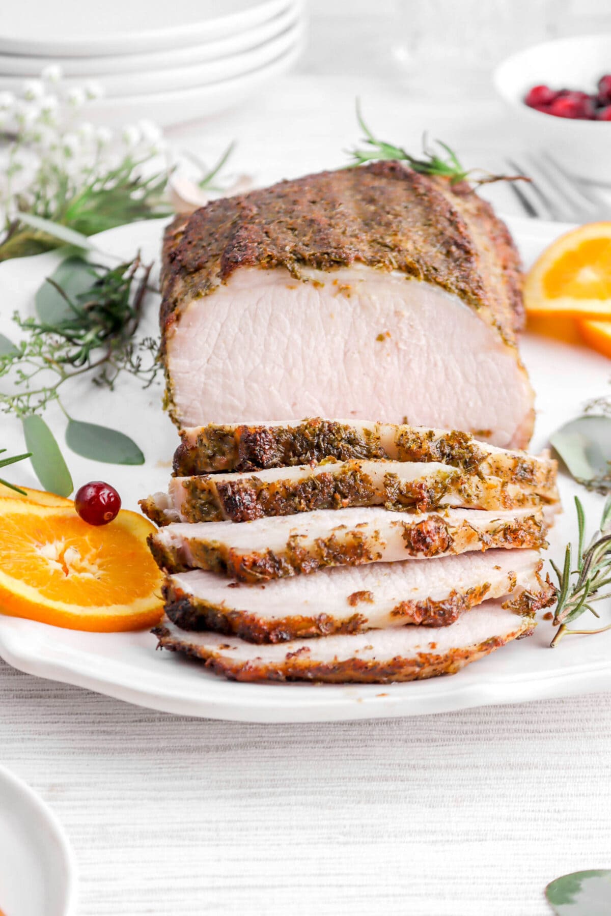 close up of pork tenderloin with five slices laying in front on round platter with rosemary sprigs and orange slices around.