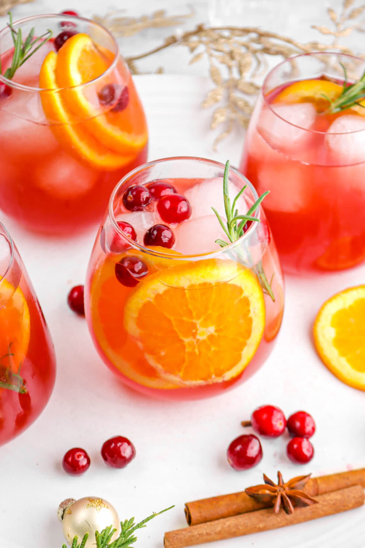 angled close up of christmas punch in glass with cranberries, orange slices, and rosemary sprig inside with more glasses around.