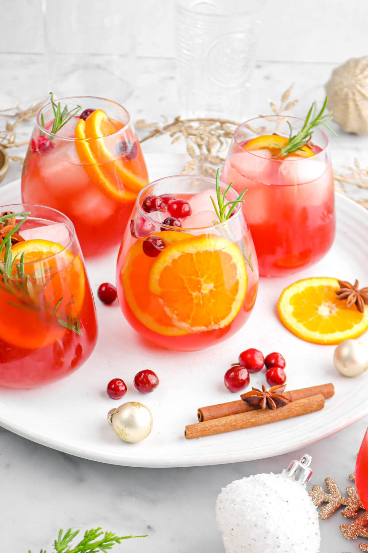 angled shot of four glasses of spiced punch on white tray with cinnamon sticks, star anise, slice of orange, and ornaments around.