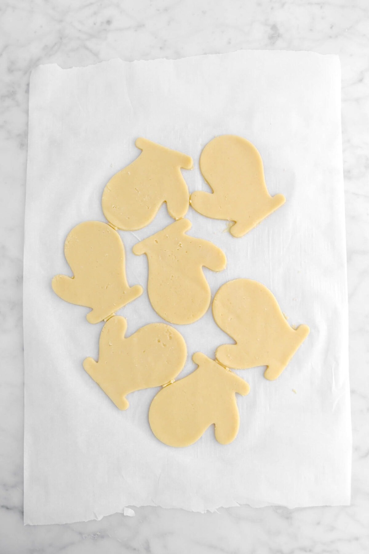 seven glove shaped unbaked cookies on parchment paper.