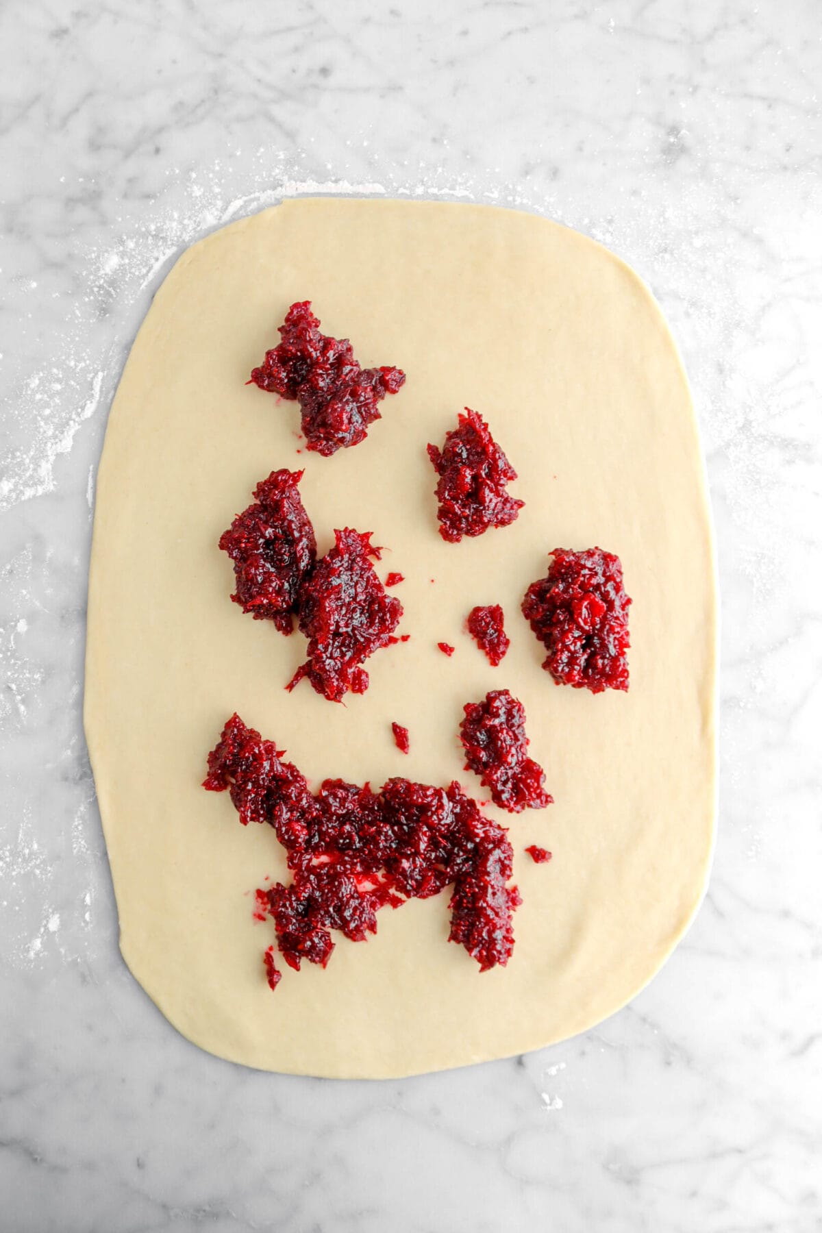 dollops of cranberry jam on rolled out sweet dough on marble surface.