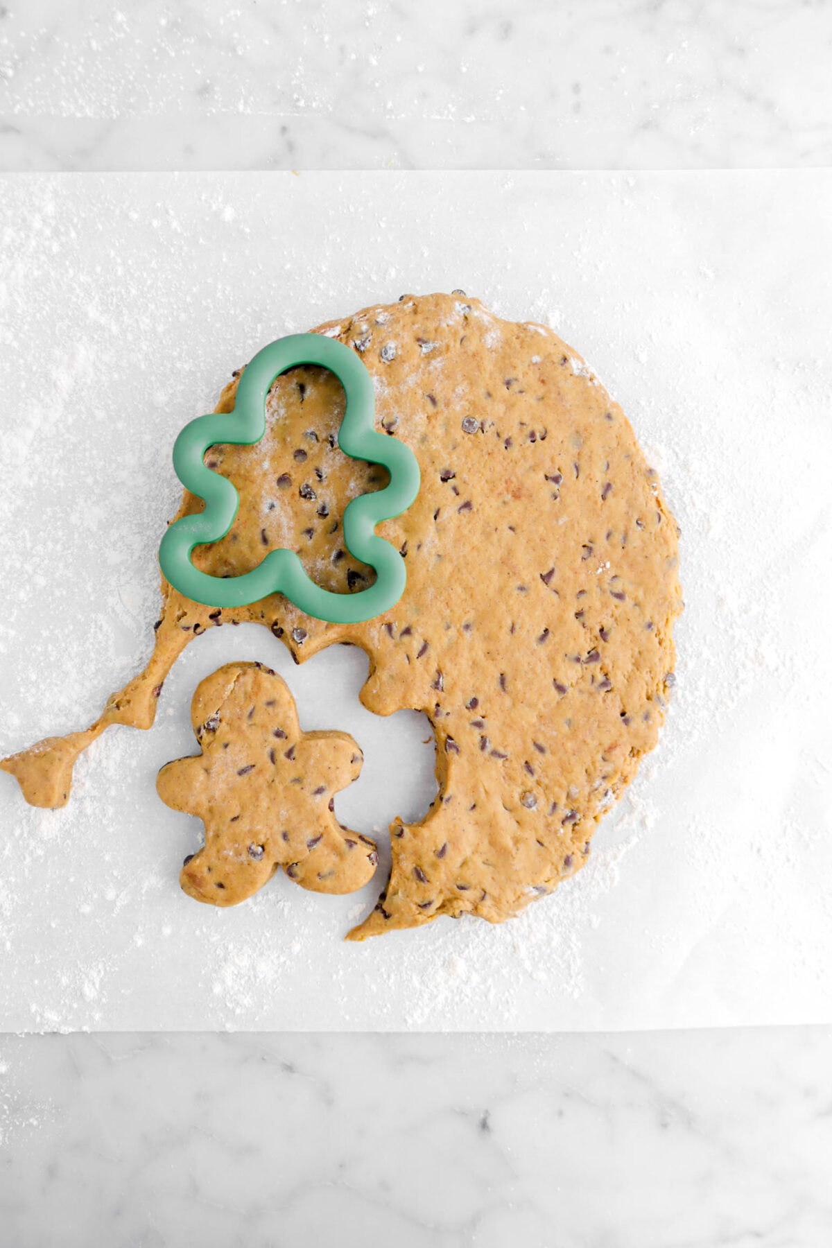 scone dough being cut into gingerbread shapes with green cookie cutter.