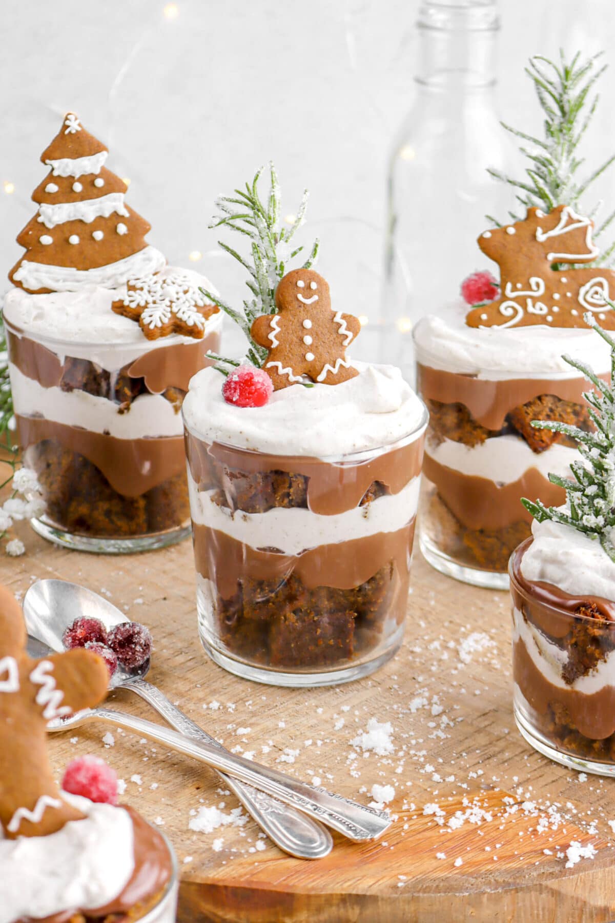 mini gingerbread trifles on wood board with gingerbread cookie decoration, sugared rosemary, and sugared cranberries on top.