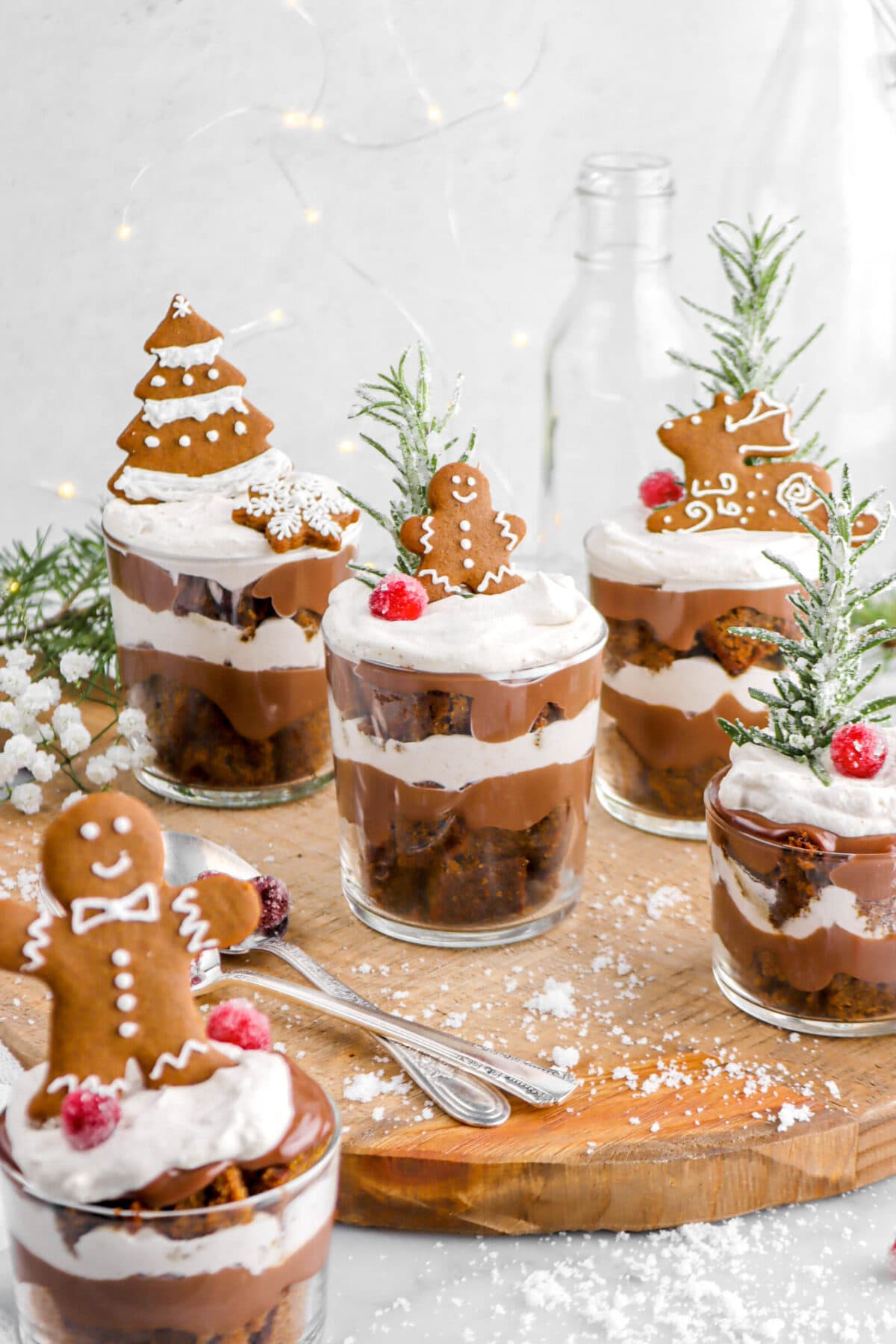 Individual gingerbread trifles with gingerbread cookies on top of each, with white flowers, and sugar around.