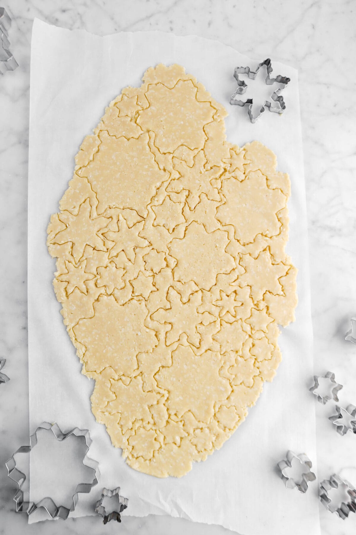 snowflakes cut into cookie dough with silver cookie cutters around.