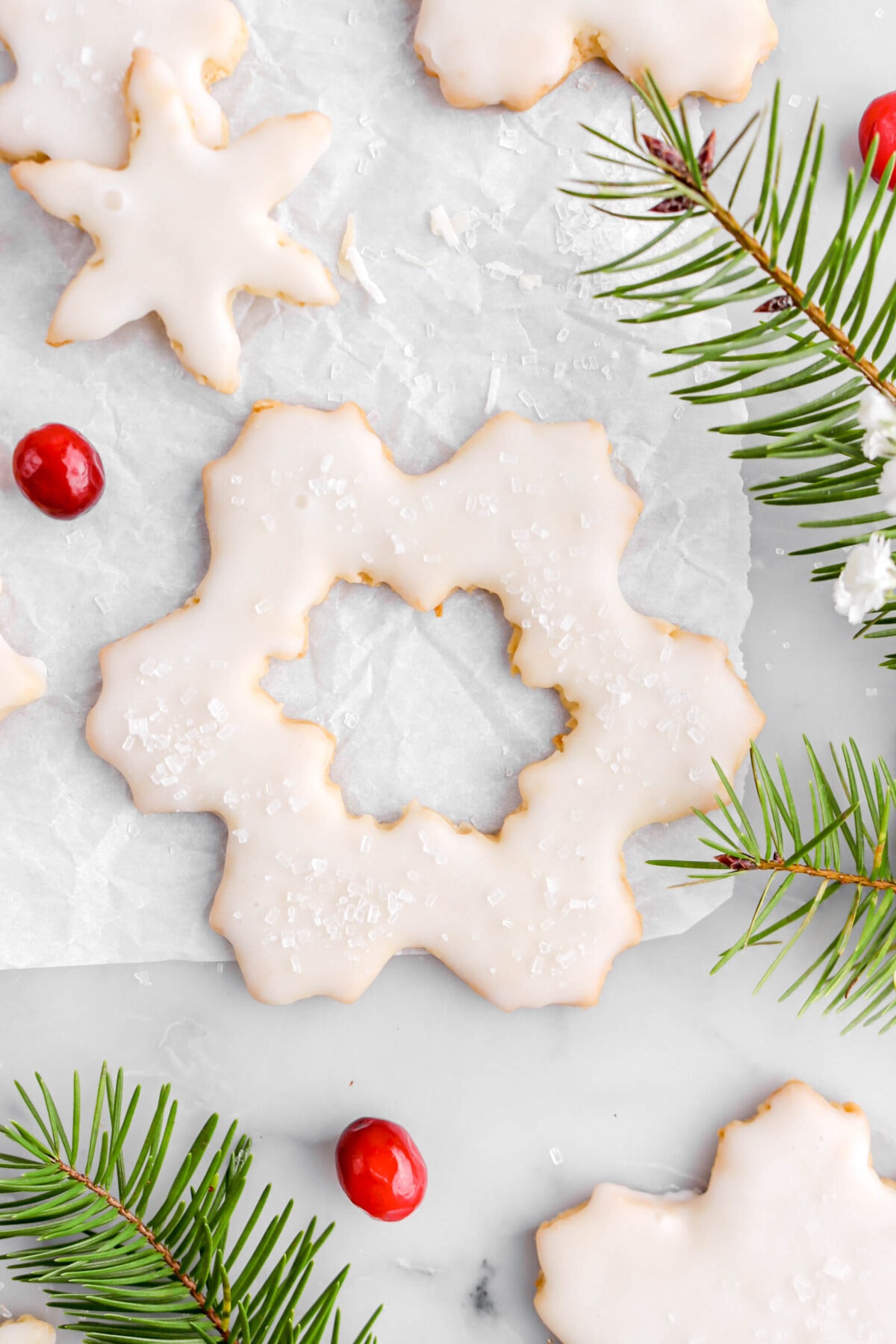 close up of large snowflake cookie with pine branch pieces around and three cranberries.