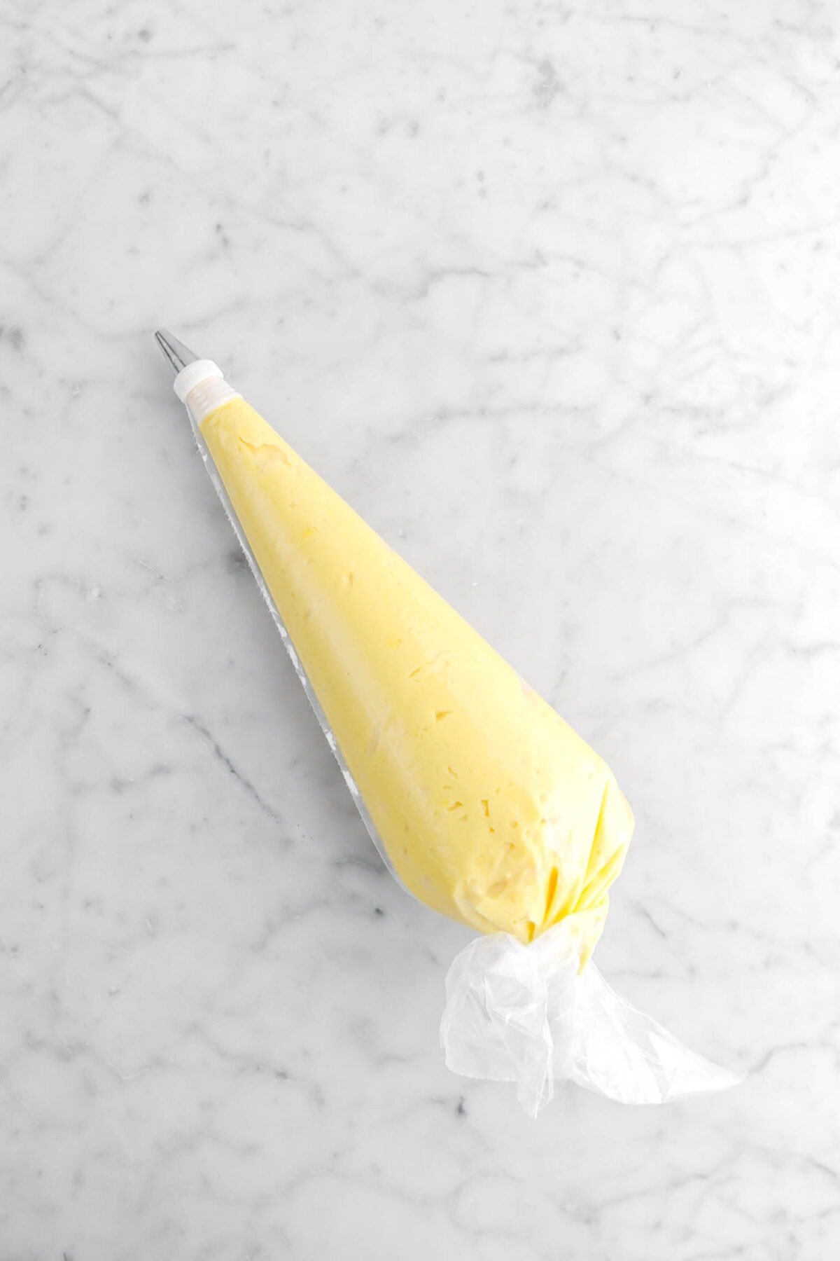 pastry cream in large piping bag on marble surface.