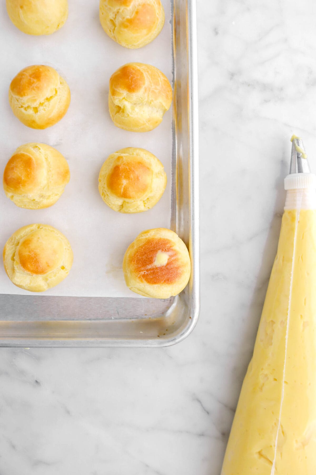 choux bun filled with pastry cream with piping bag of pastry cream beside.