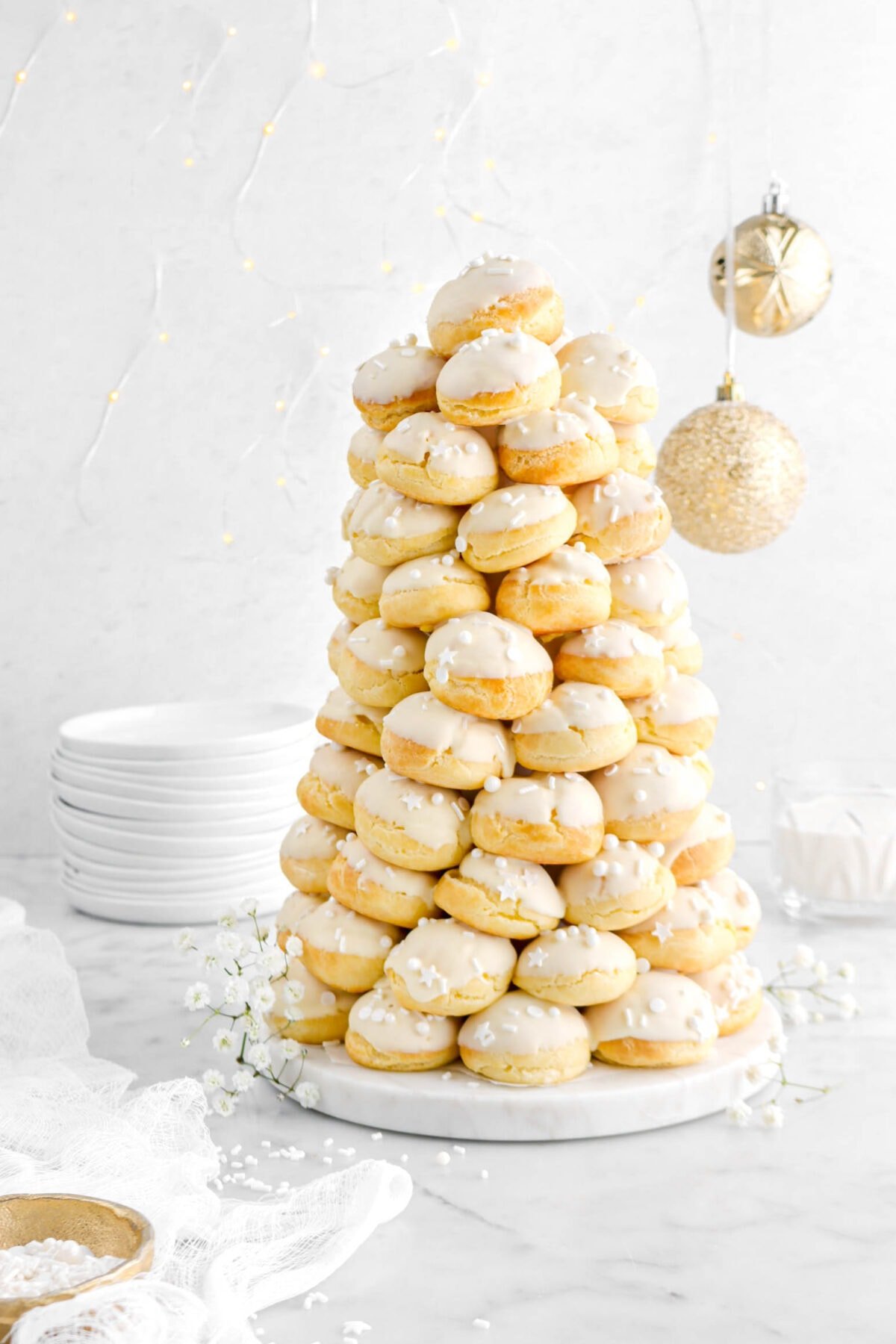 croquembouche off-center with two gold ornaments behind and stack of plates.