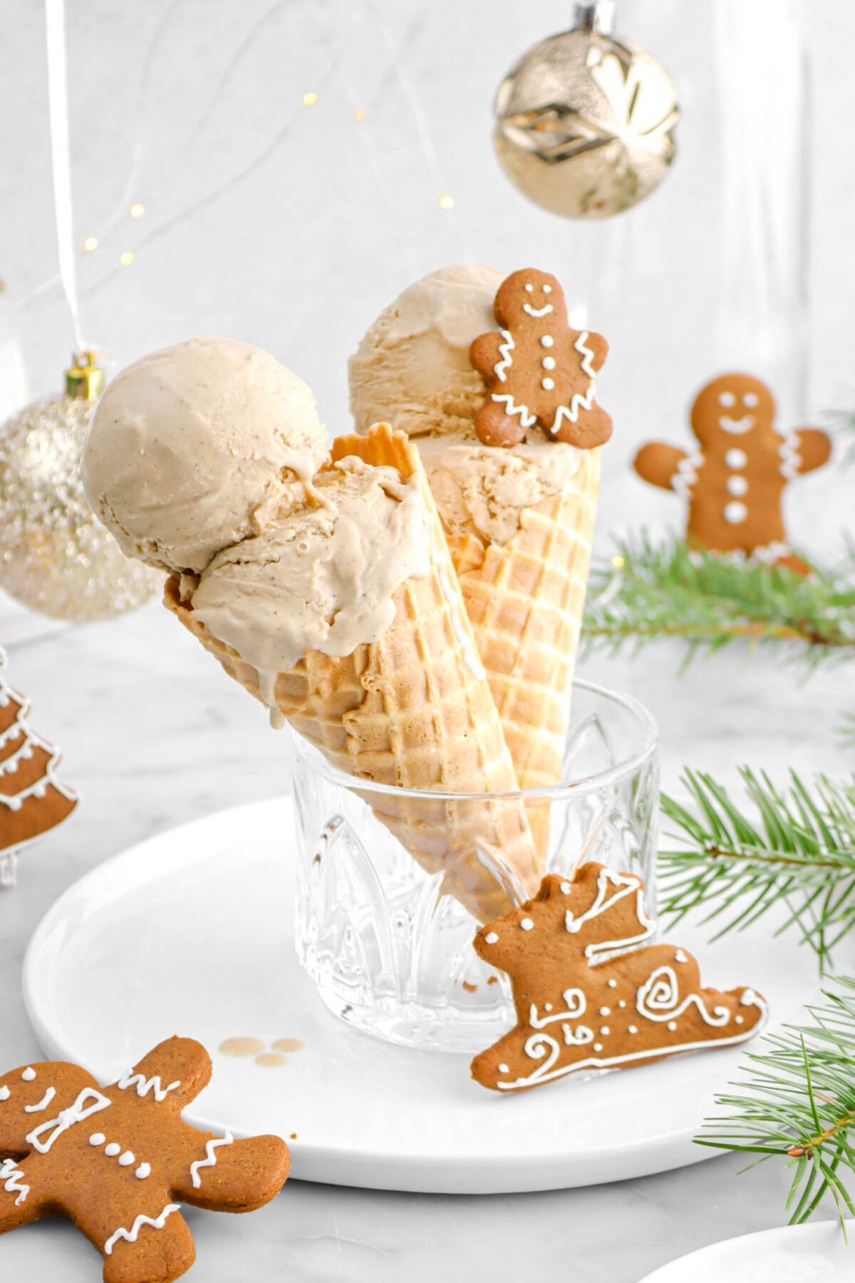 close up of two ice cream cones with two scoops of gingerbread ice cream each, with a mini gingerbread cookie on the back cone.