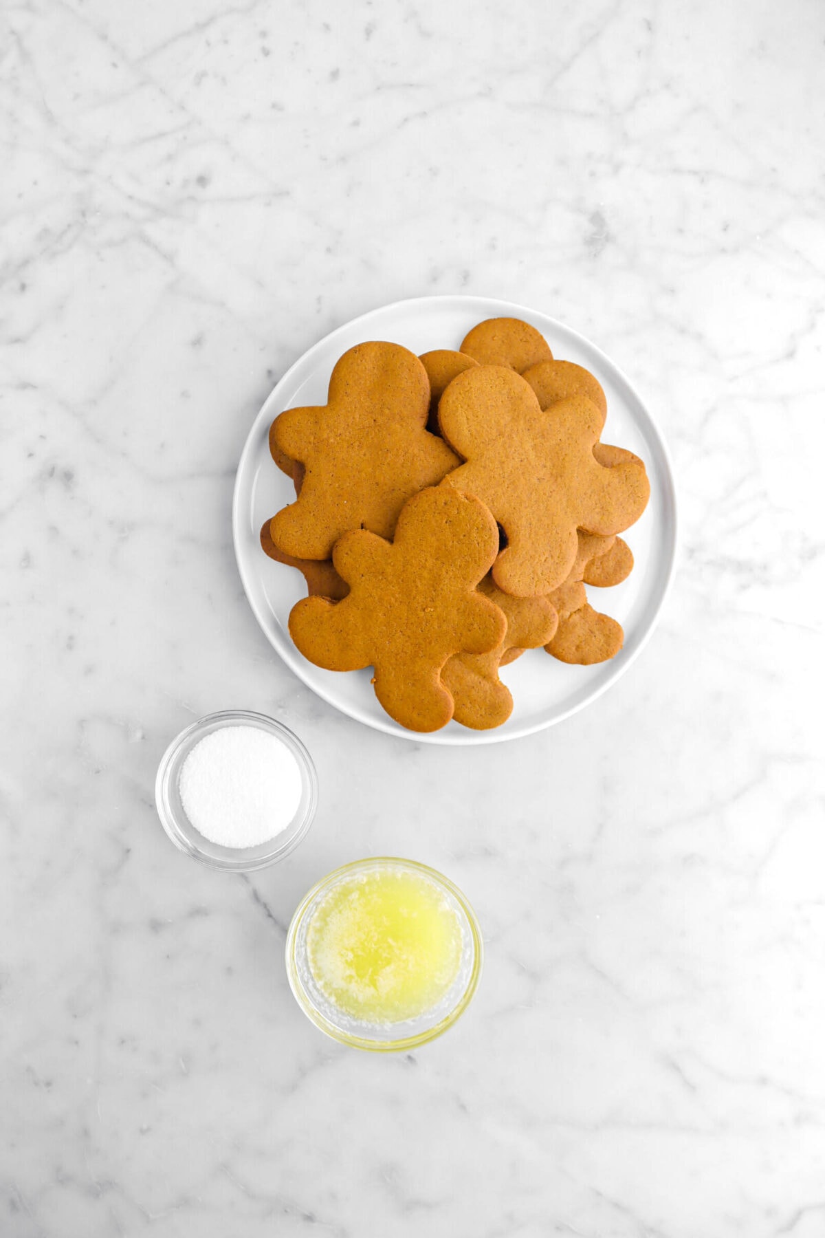 gingerbread cookies, granulated sugar, and melted butter on marble surface.