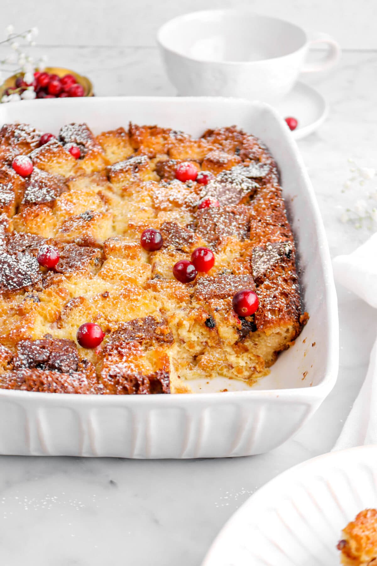 angled close up of slice missing from bread pudding with fresh cranberries on top and powdered sugar.
