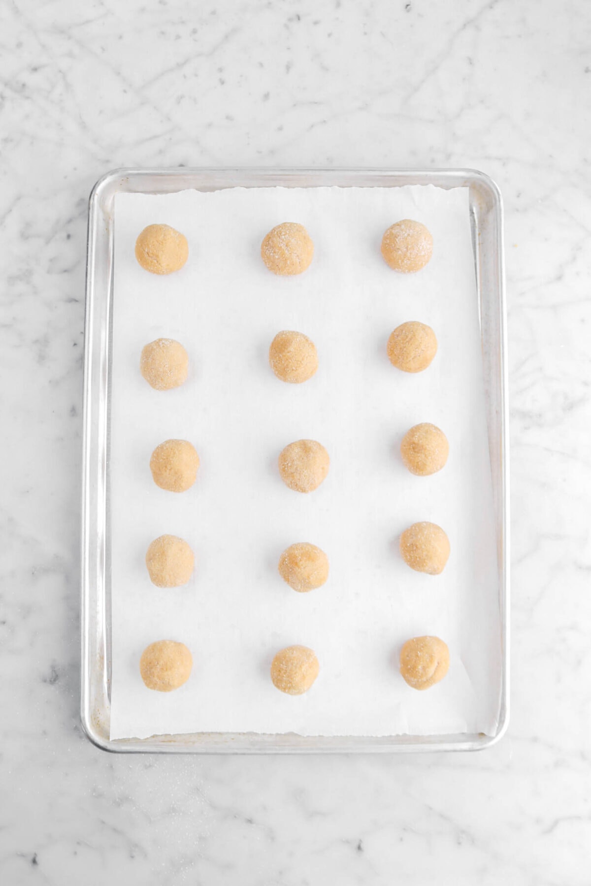 fifteen cookie dough balls on lined sheet pan.