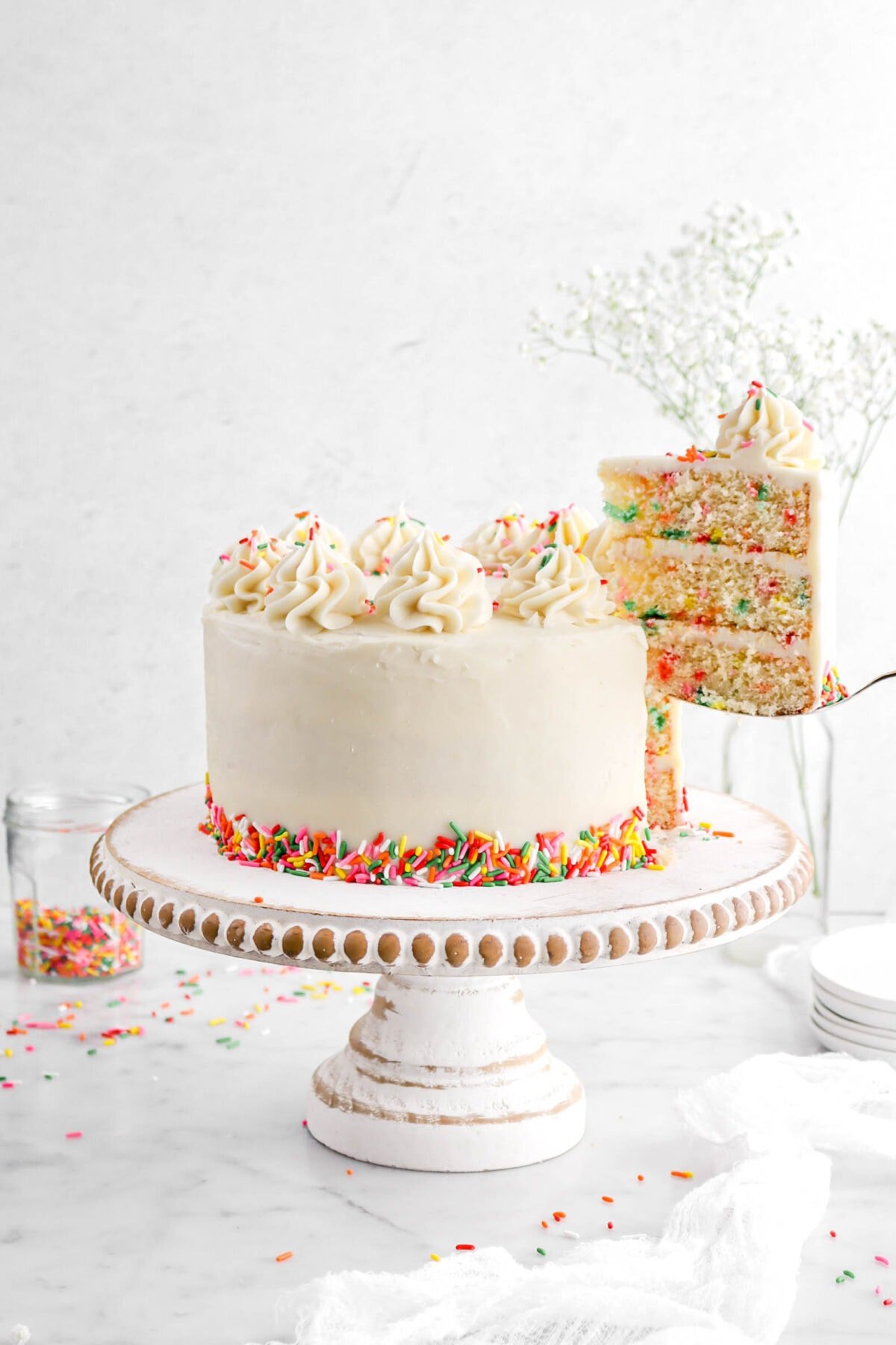 slice of funfetti cake being lifted away from cake on wood cake stand.