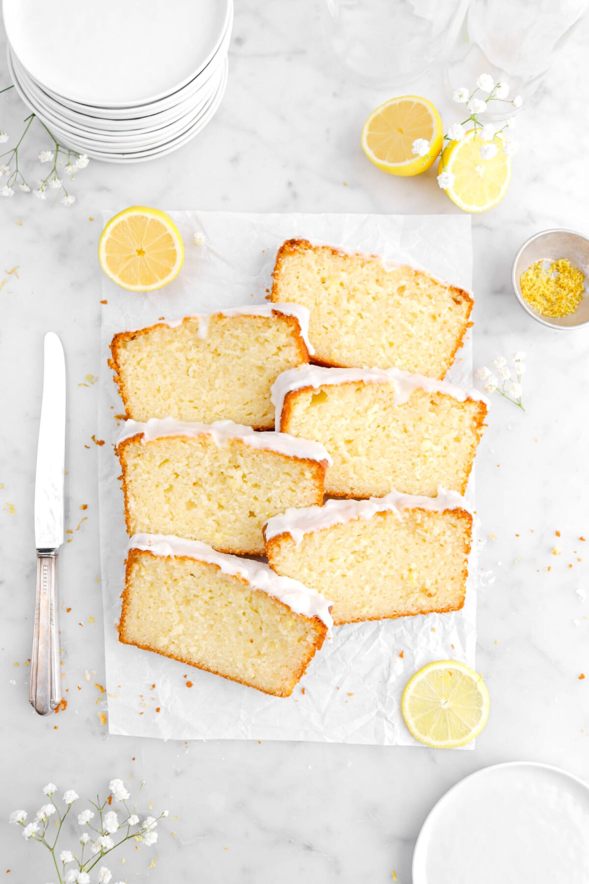 six slices of lemon loaf cake on parchment paper with flowers and lemons around.