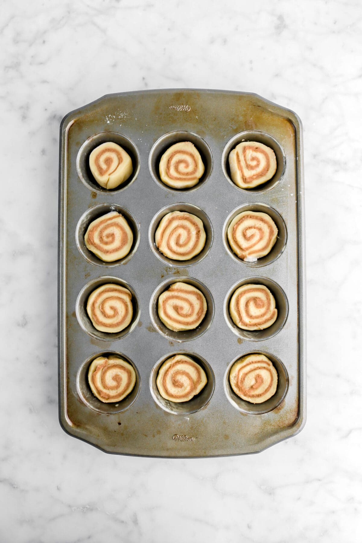 twelve unbaked cinnamon rolls in muffin pan.