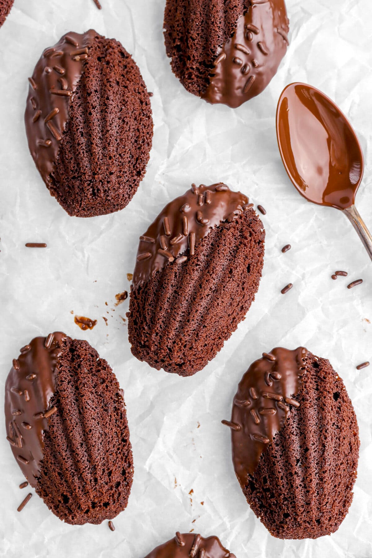 close up of chocolate dipped madeleines on parchment paper with chocolate coated spoon beside.