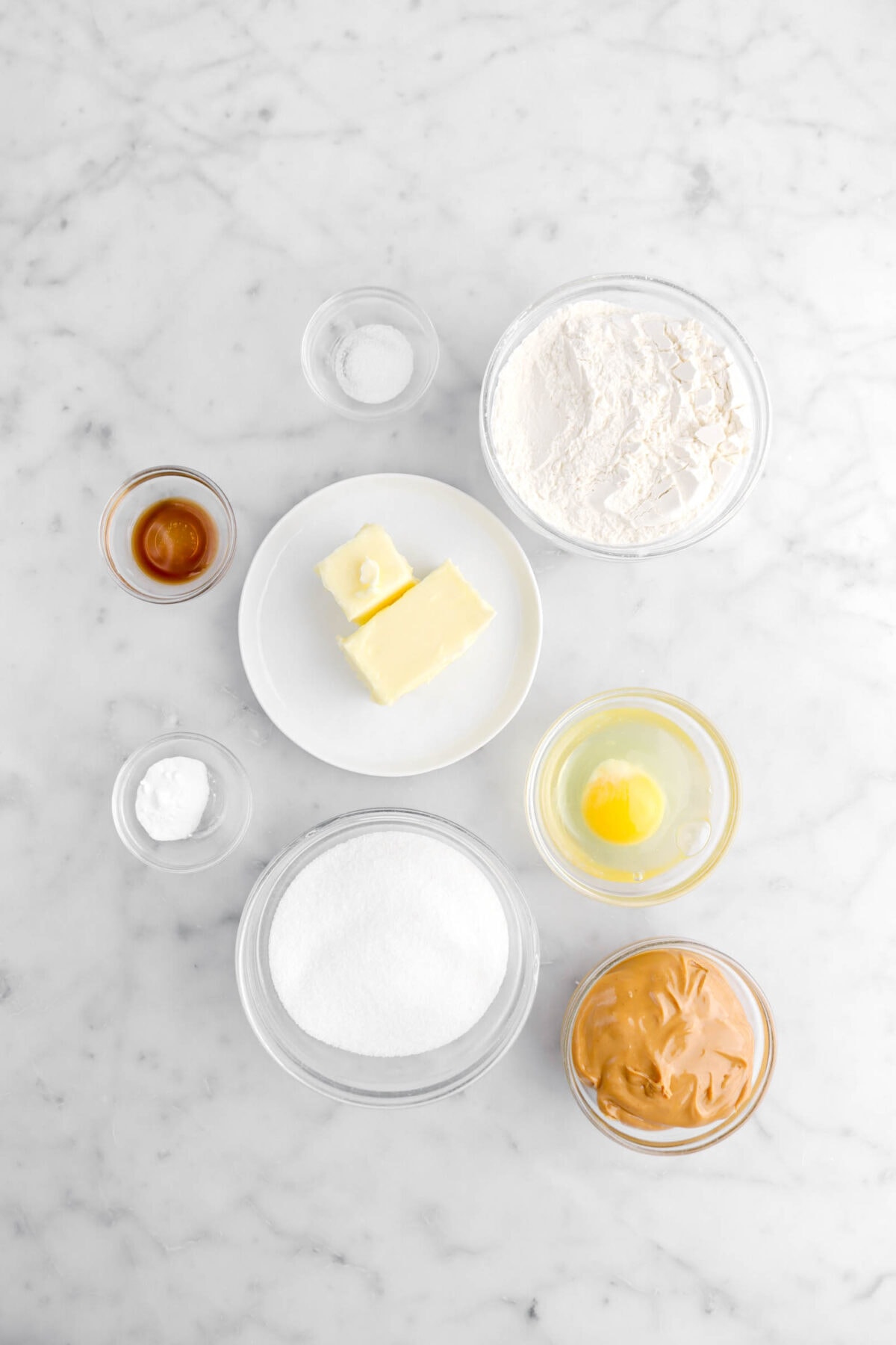 salt, flour, butter, vanilla, baking soda, egg, sugar, and creamy peanut butter on marble surface.