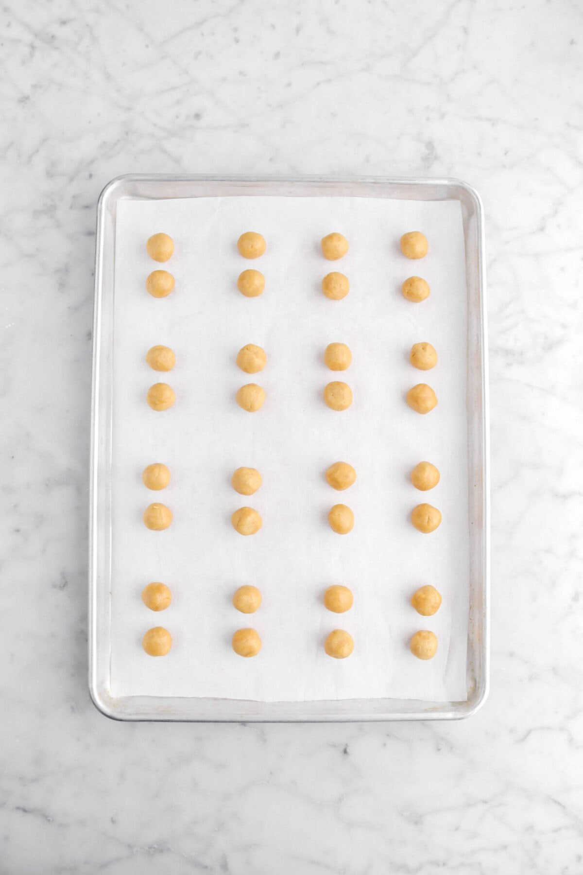 32 small balls of peanut butter cookie dough on lined sheet pan.
