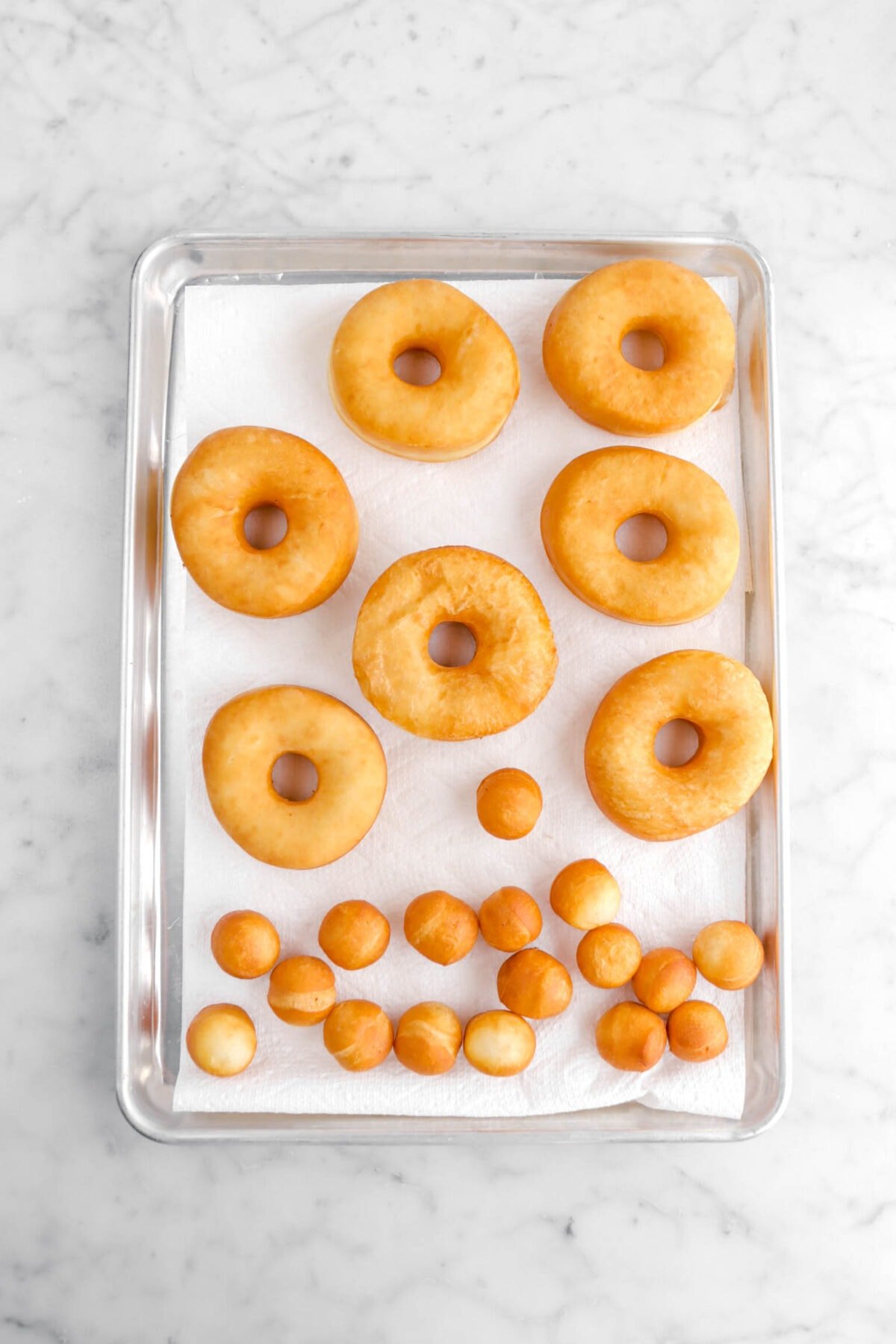 fried doughnuts and doughnut holes on paper towel lined sheet pan.