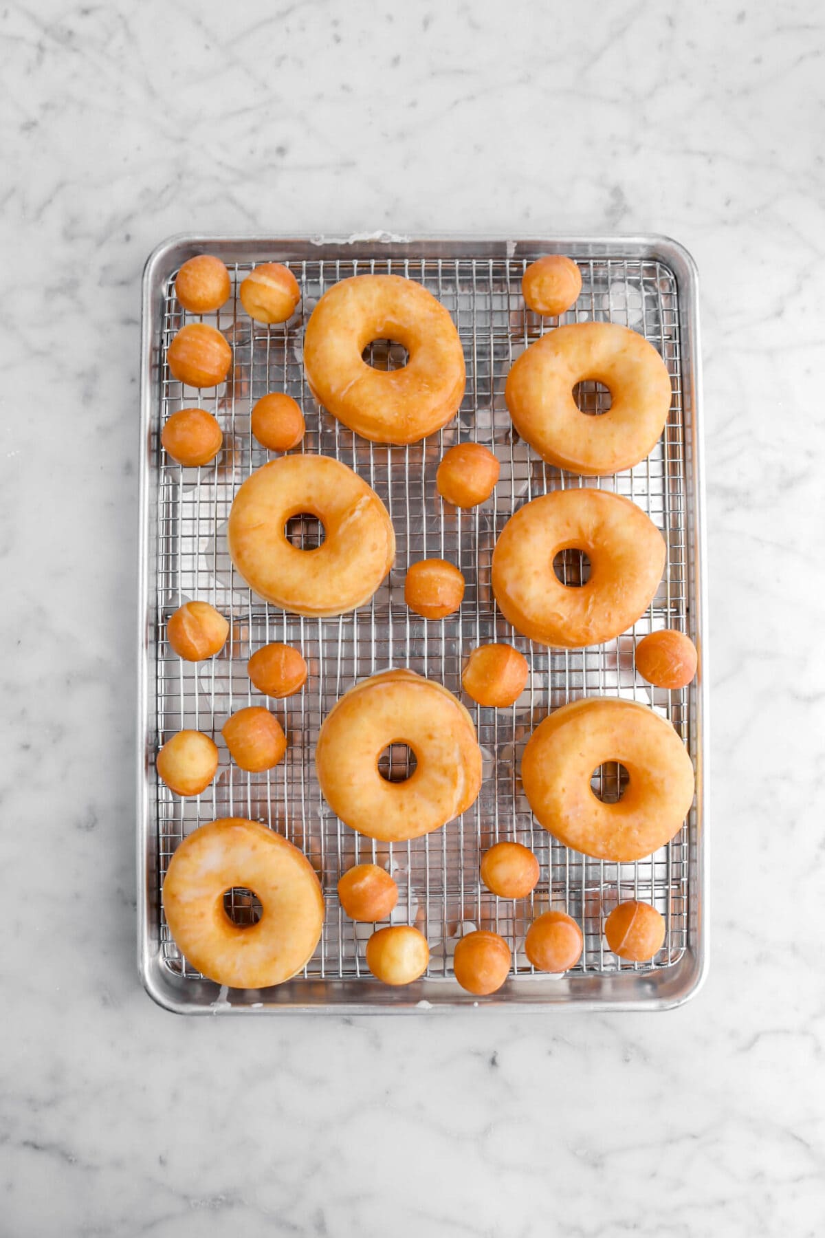 glaze coated doughnuts and doughnut holes on cooling rack in sheet pan.