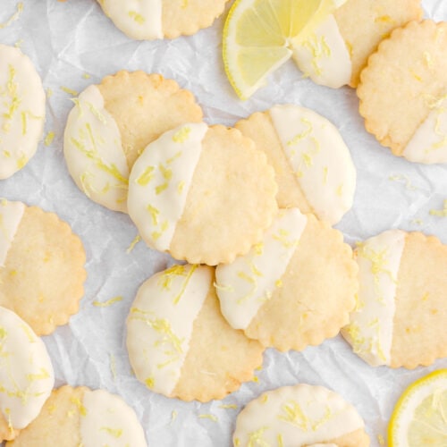 lemon shortbread cookies on crumbled parchment paper with half of a lemon slice leaning on one cookie.