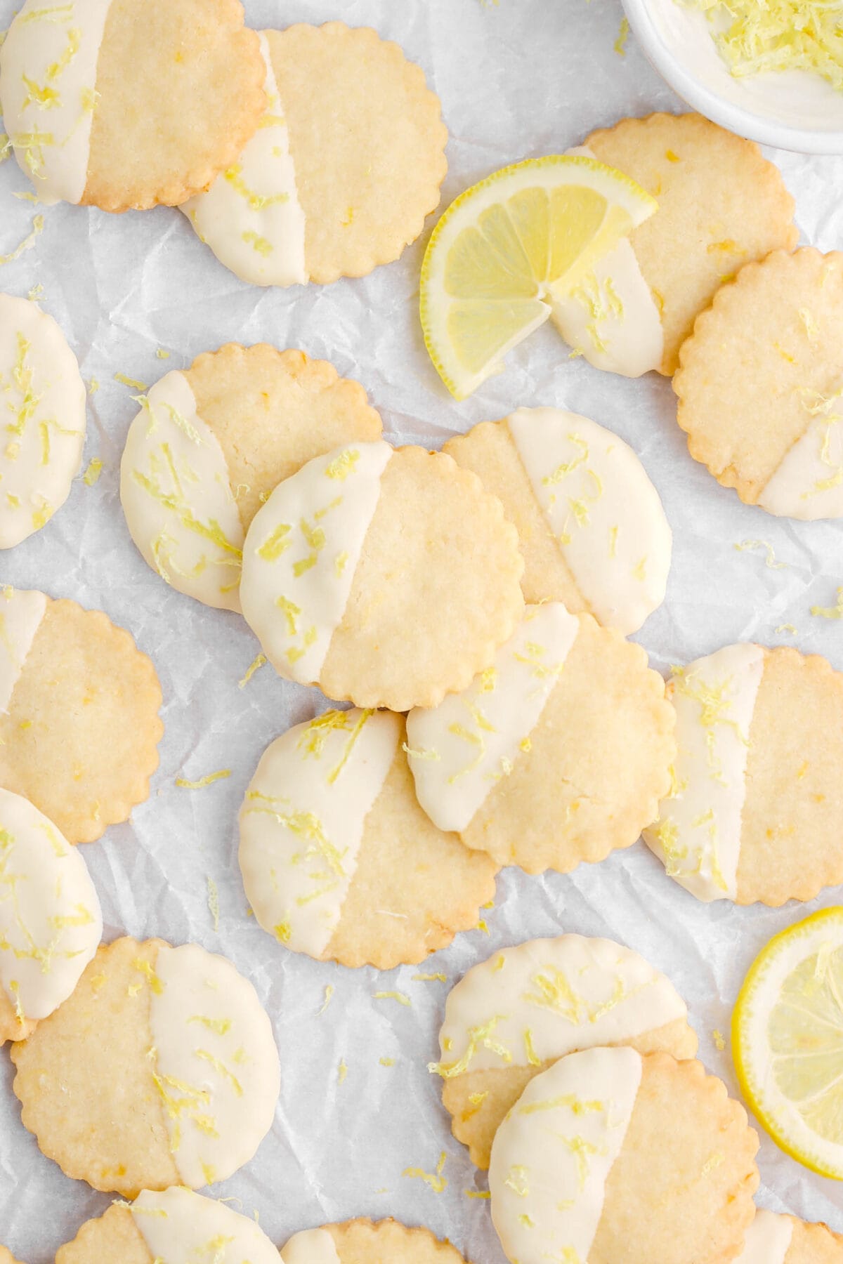 lemon shortbread cookies on crumbled parchment paper with half of a lemon slice leaning on one cookie.