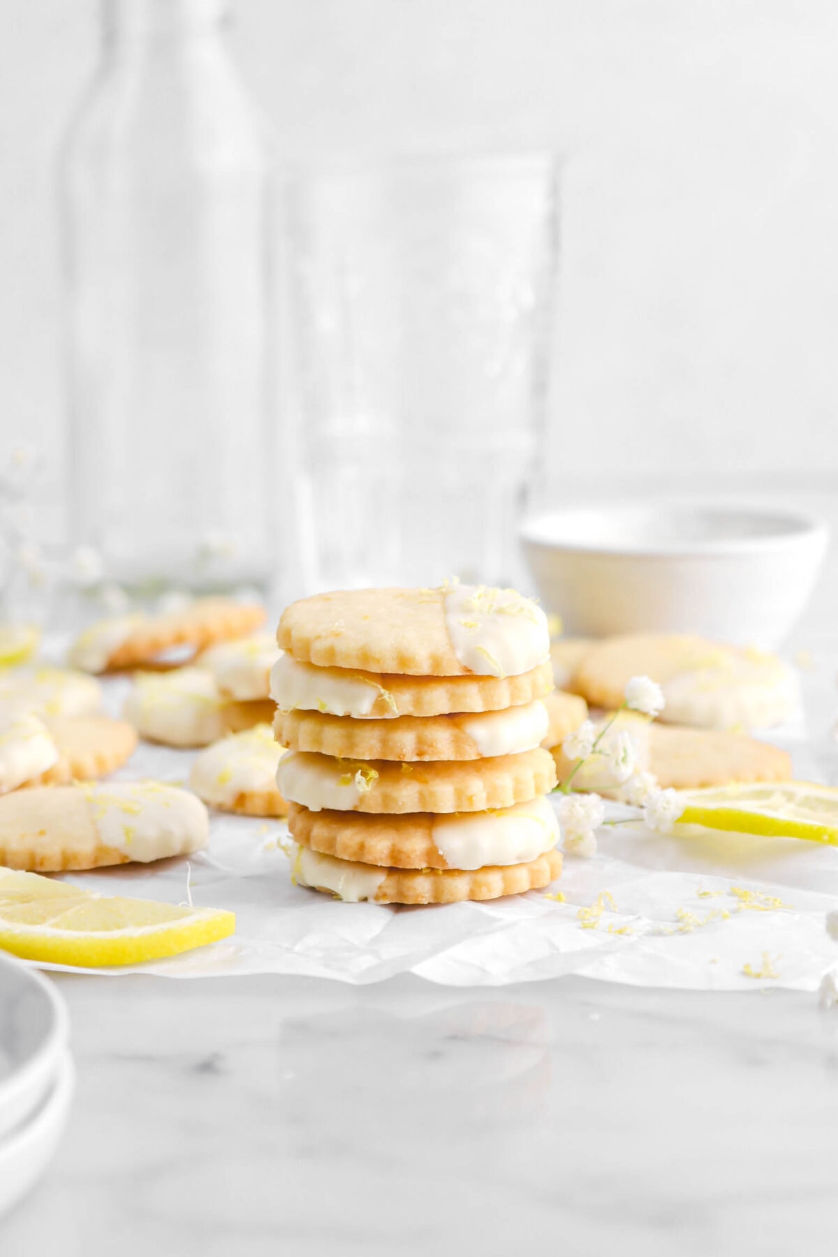 stacked lemon shortbread cookies on parchment paper with more cookies behind.