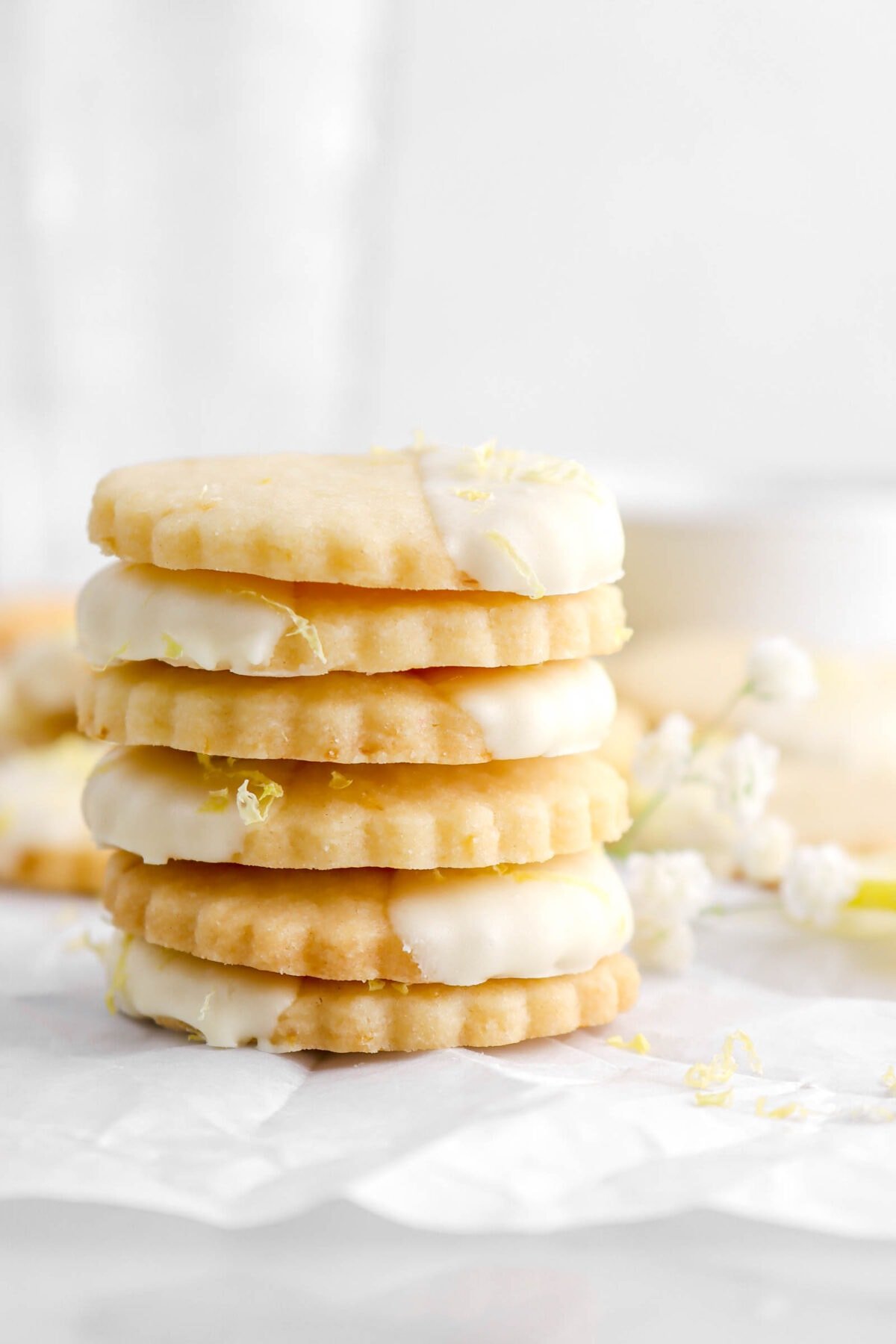 close up of stacked lemon shortbread cookies on parchment paper with white flowers beside.