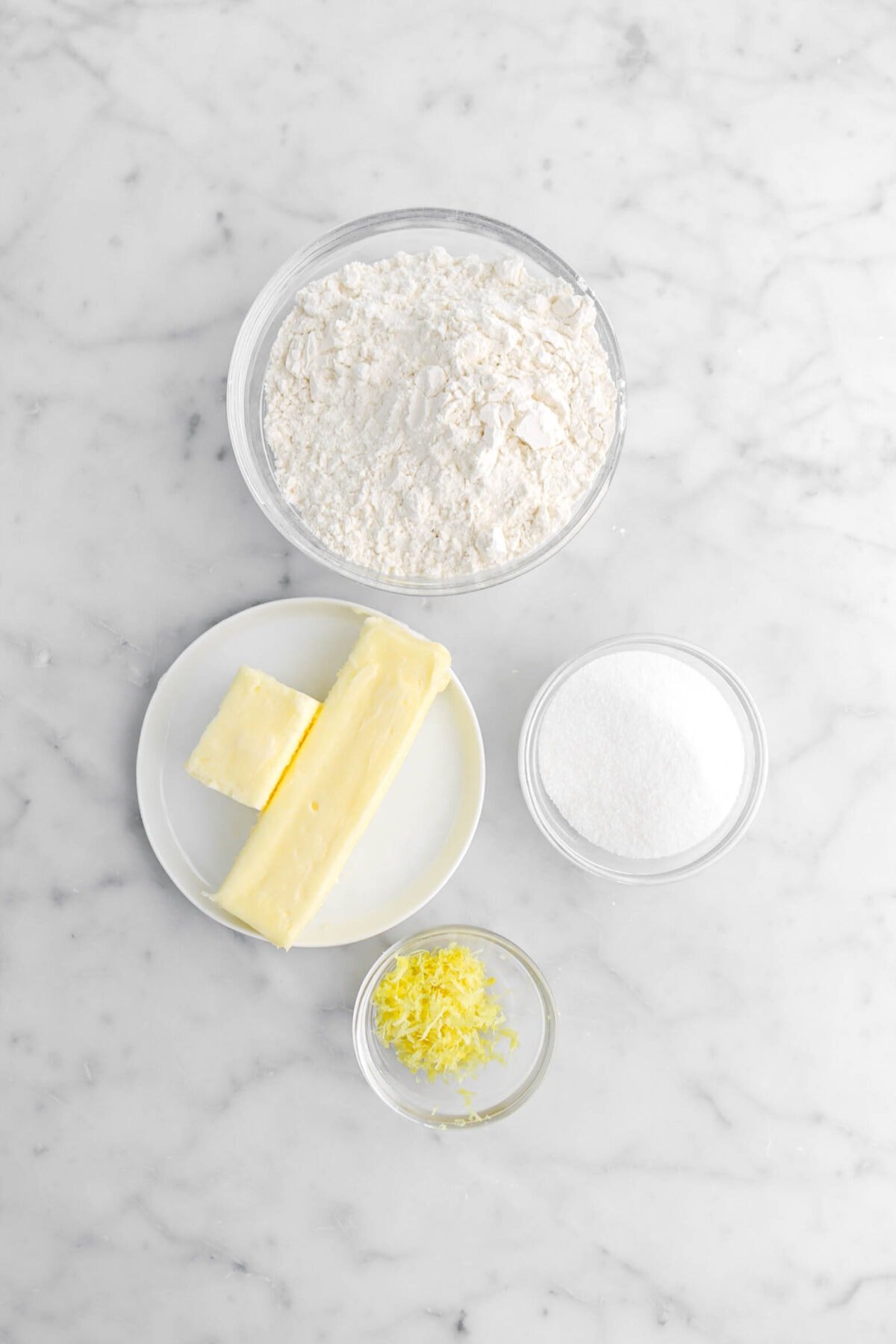 flour, sugar, butter, and lemon zest on marble surface.